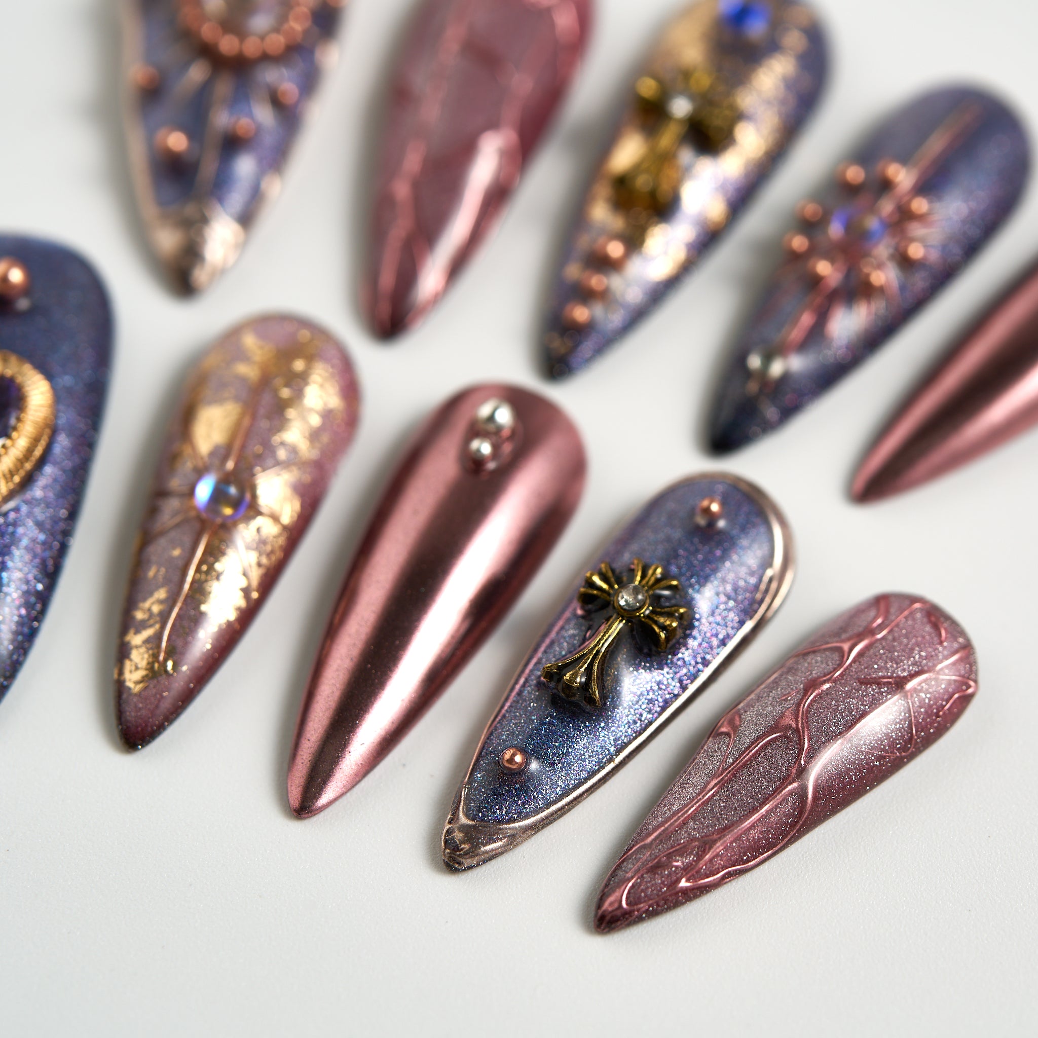 Detail view of Violet Eclipse metallic purple and gold stiletto reusable press-on nails, showcasing nail art with charms