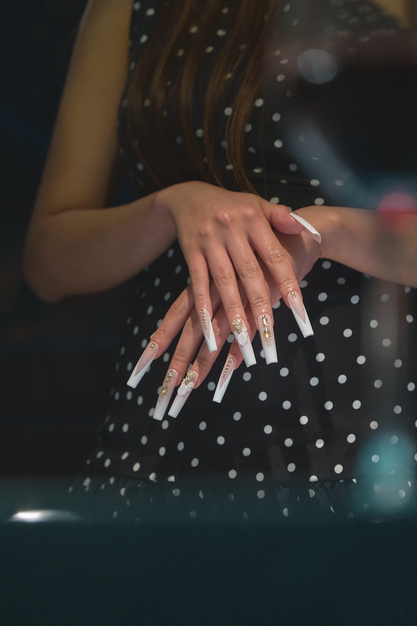 full view of long square nails in blush pink and white with gold accents and 3D bow shown on both hands against a dark background