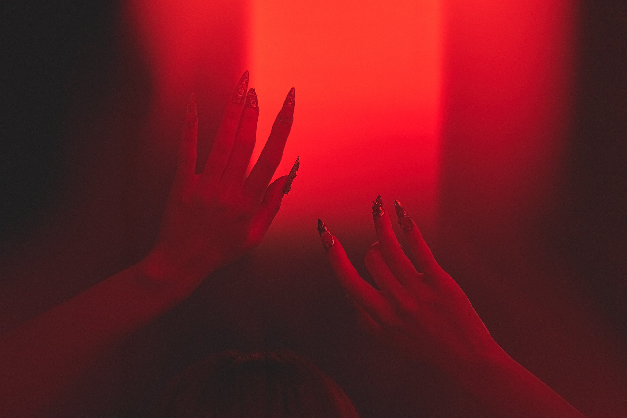 Chrome Reign stiletto press-on nails in metallic chrome silver, hands reaching in dramatic red lighting, high-impact manicure for nightlife or editorial styling