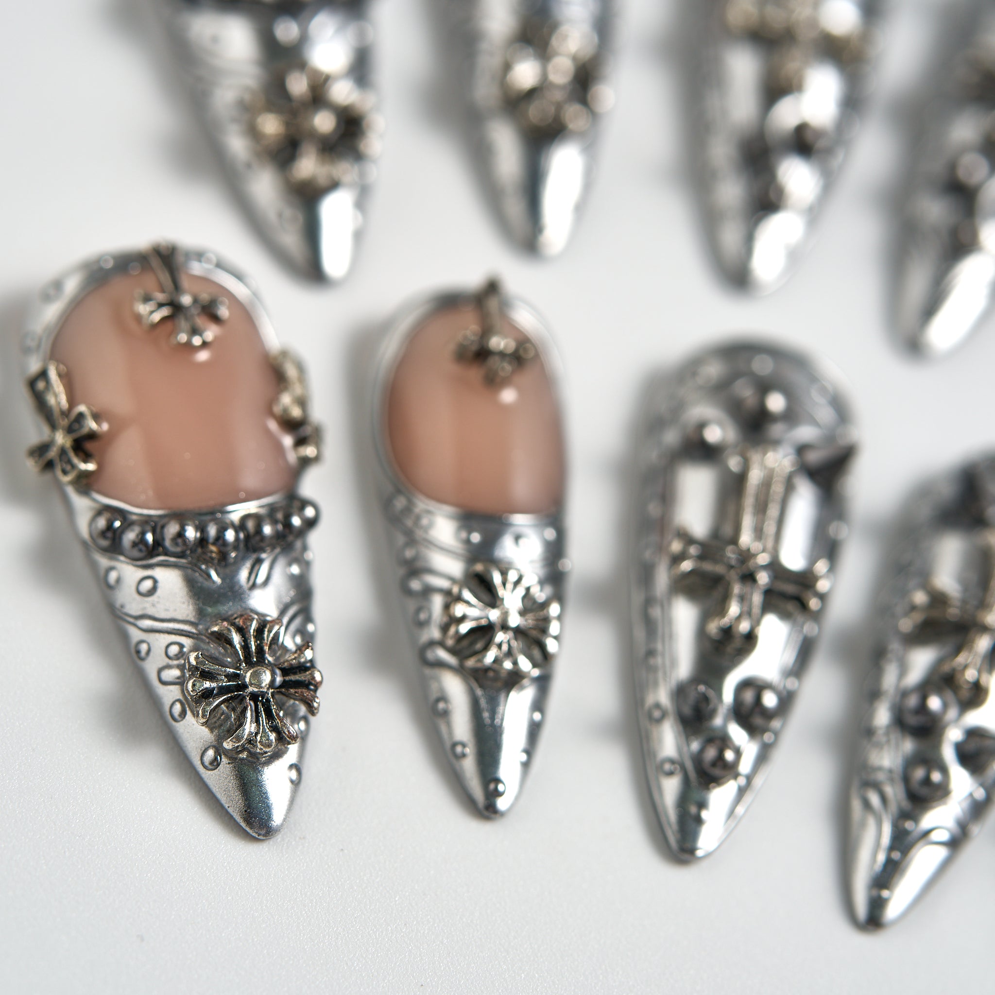Chrome Reign stiletto press-on nails in metallic chrome silver, ultra close-up showing 3D floral and cross embellishments on a white background