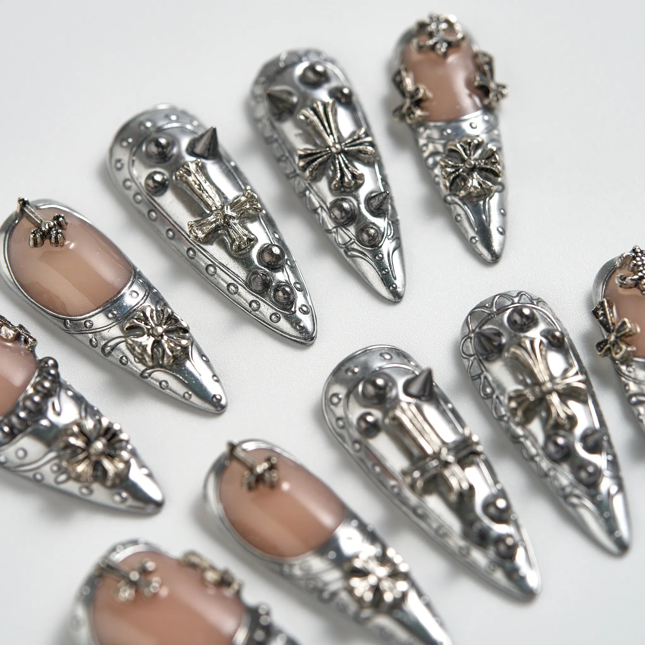Decorative nail art with silver embellishments and beige nail polish on a white background