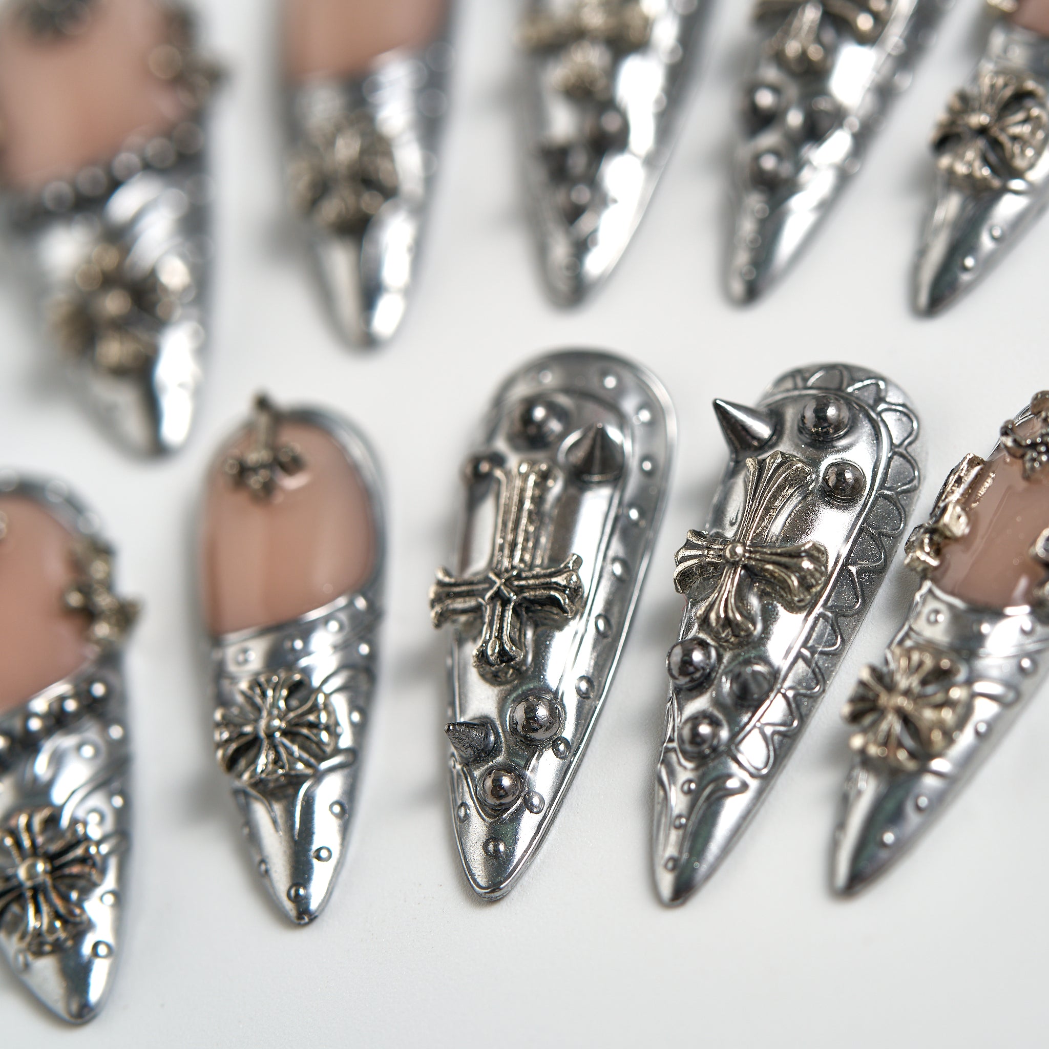 Chrome Reign stiletto press-on nails in metallic chrome silver, macro detail of reusable nails with 3D cross and studded embellishments on a white background