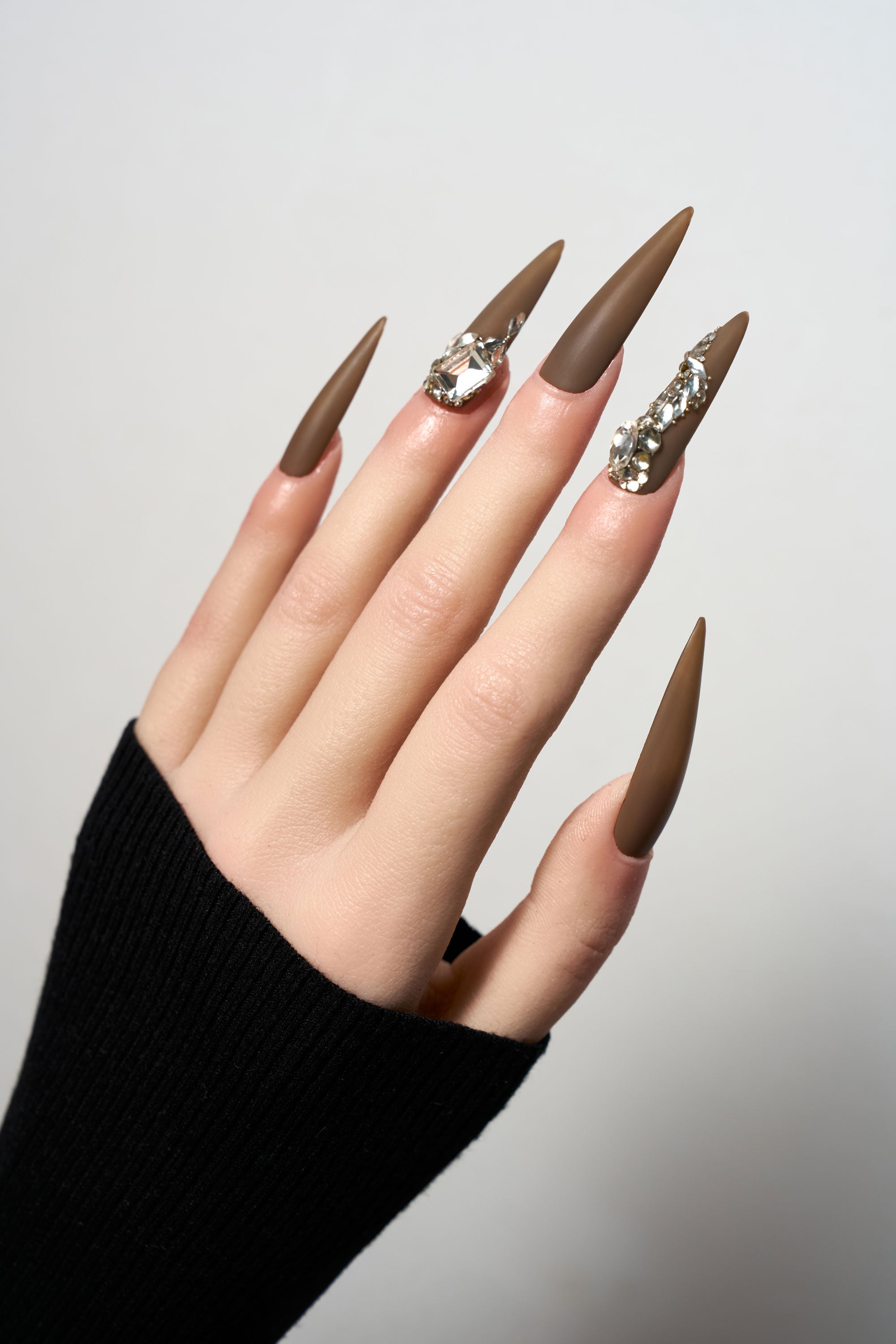 Desert Halo reusable long stiletto press-on nails in a sophisticated matte chocolate brown finish, heavily adorned with luxury clear crystal trails and large focal gemstones.