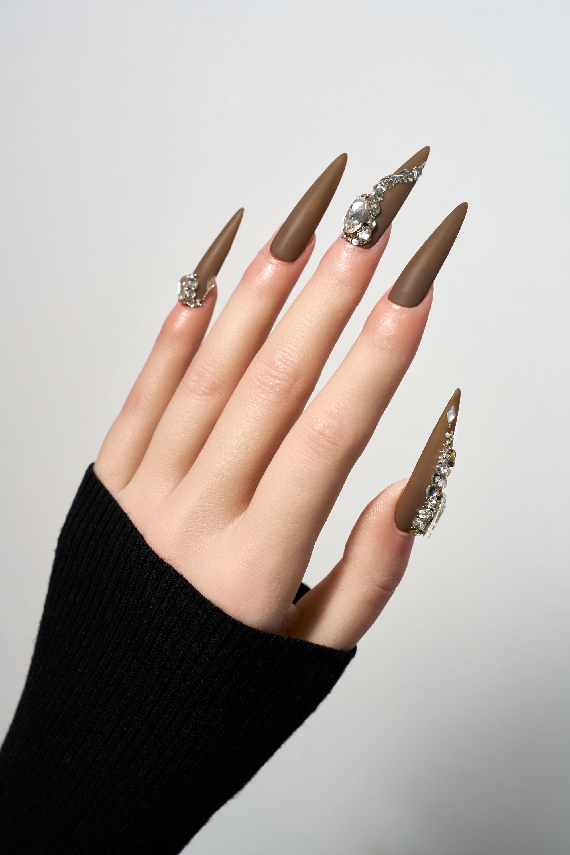 Desert Halo reusable long stiletto press-on nails in a sophisticated matte chocolate brown finish, heavily adorned with luxury clear crystal trails and large focal gemstones.