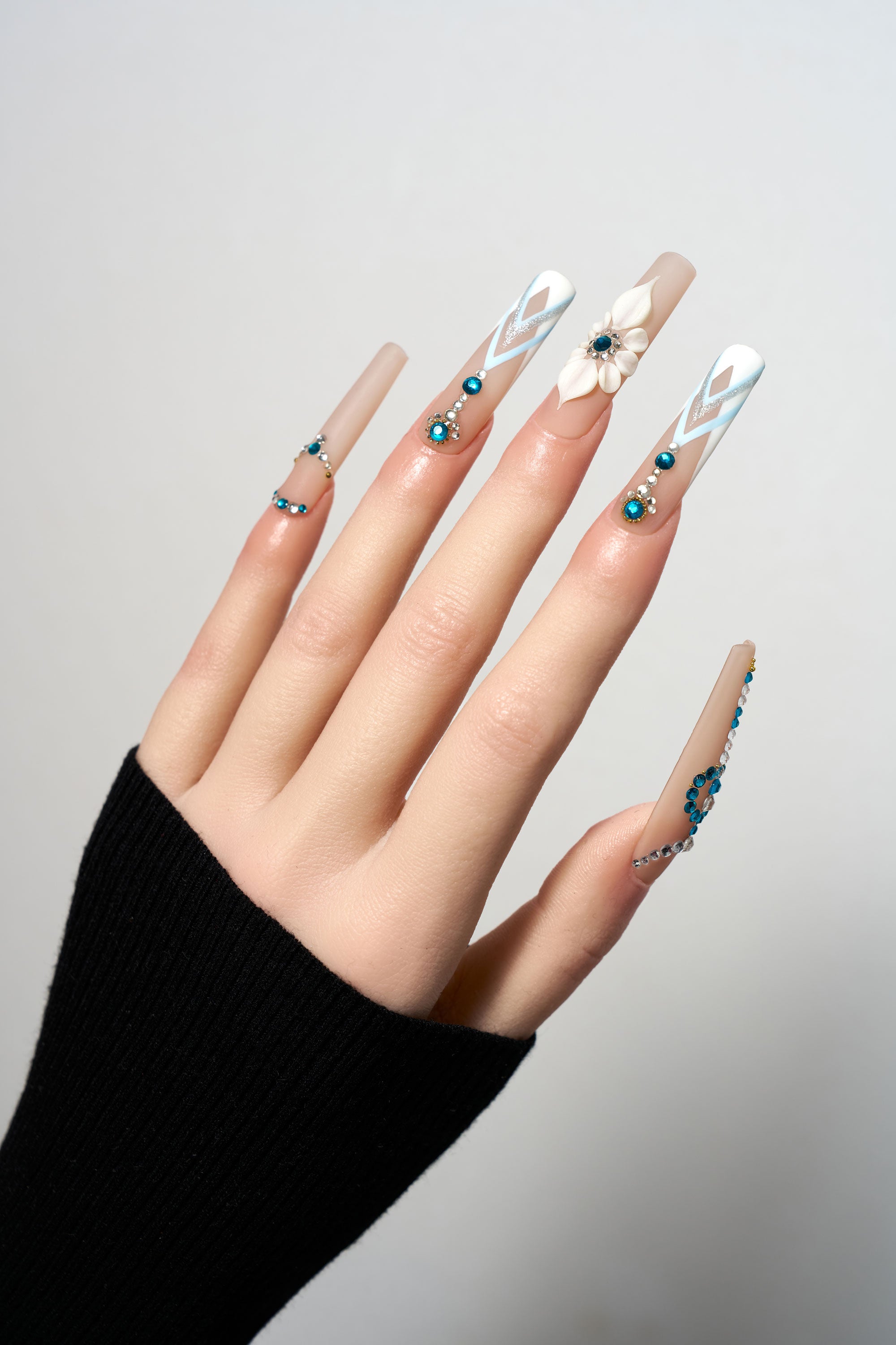 Frost Waltz reusable extra-long coffin press-on nails featuring a nude base with blue crystal trails, 3D white flower accents, and geometric silver and blue gemstone patterns.