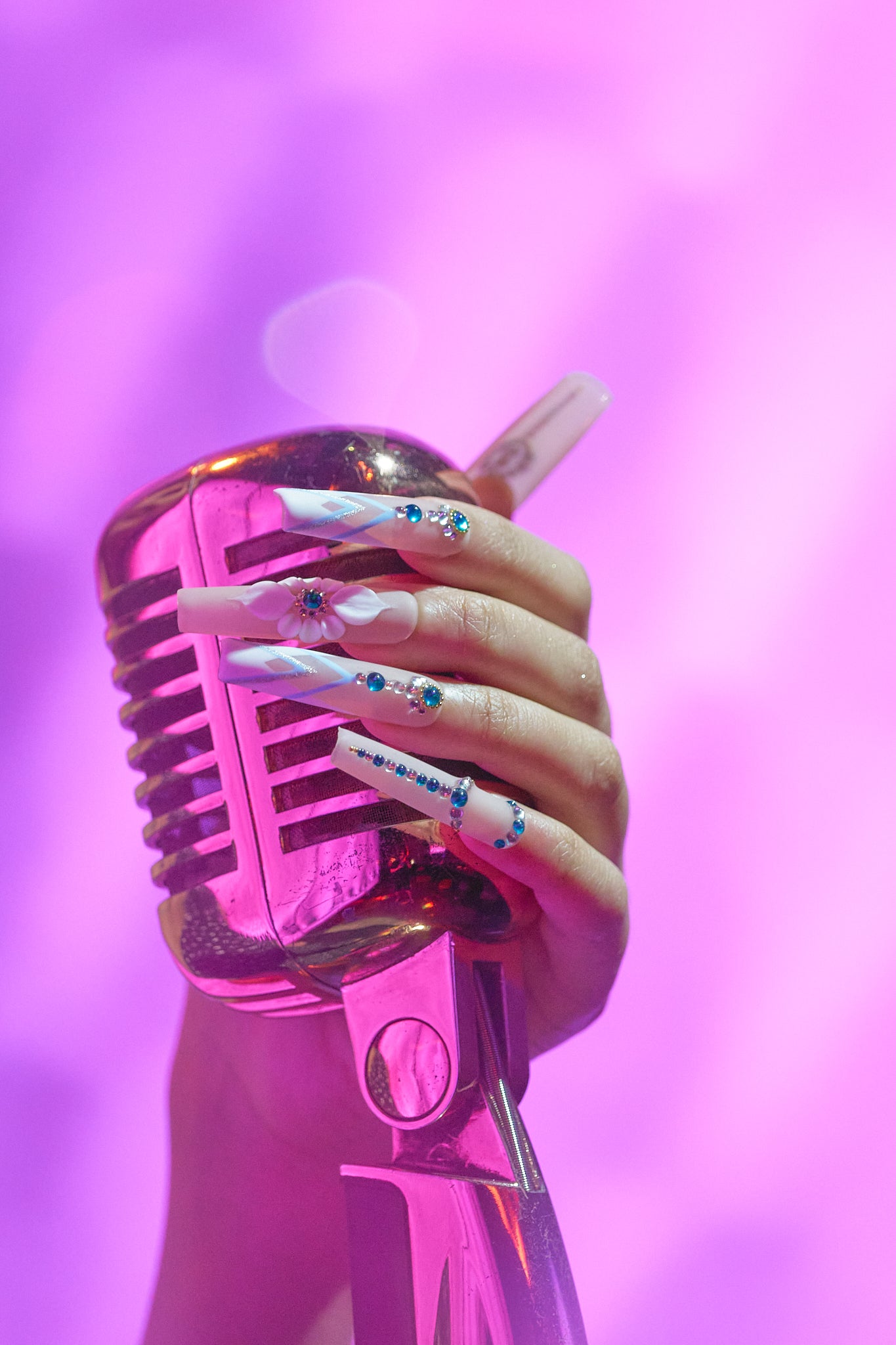 Hand with ‘Frost Waltz’ long square press-on nails holding a vintage pink microphone against a soft spotlight-pink background.