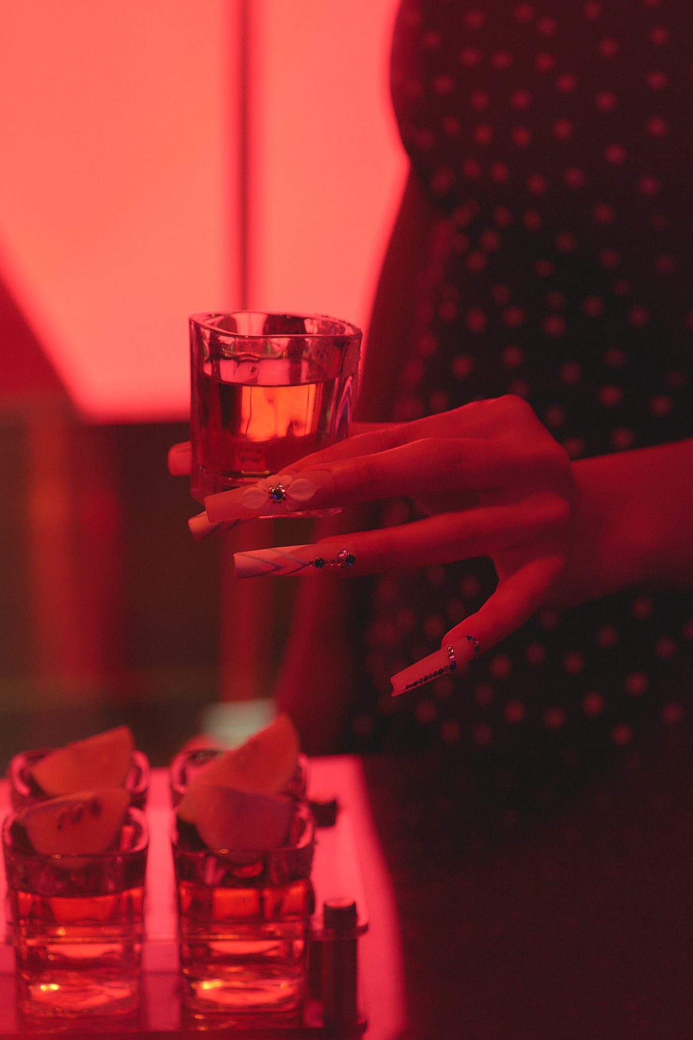 Hand with ‘Frost Waltz’ long square press-on nails holding a shot glass under red lighting at a bar, with tequila and lime in the foreground.