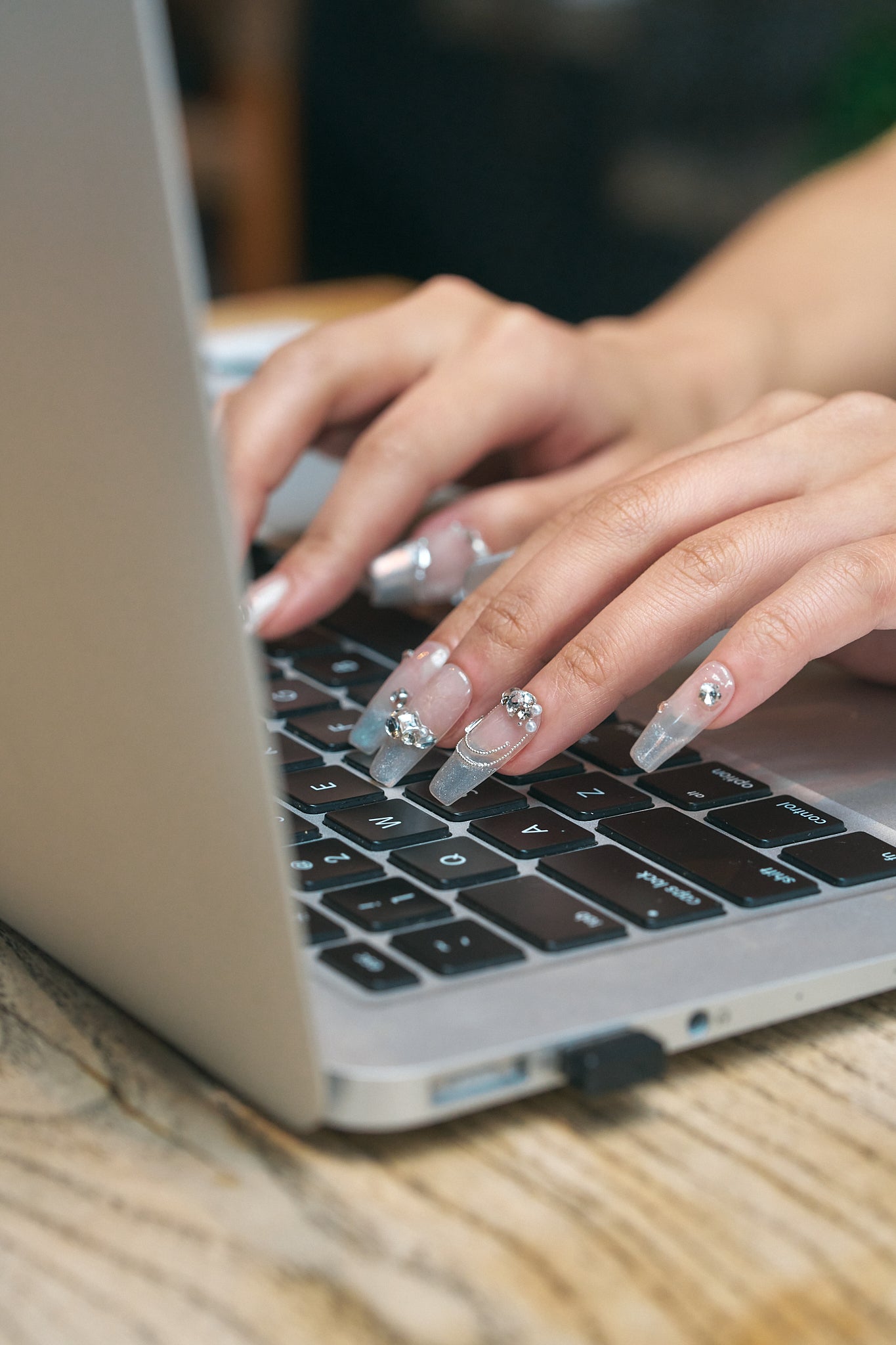 Close-up of hands wearing Gilded Heiress beige rhinestone press-on nails typing on a laptop keyboard.