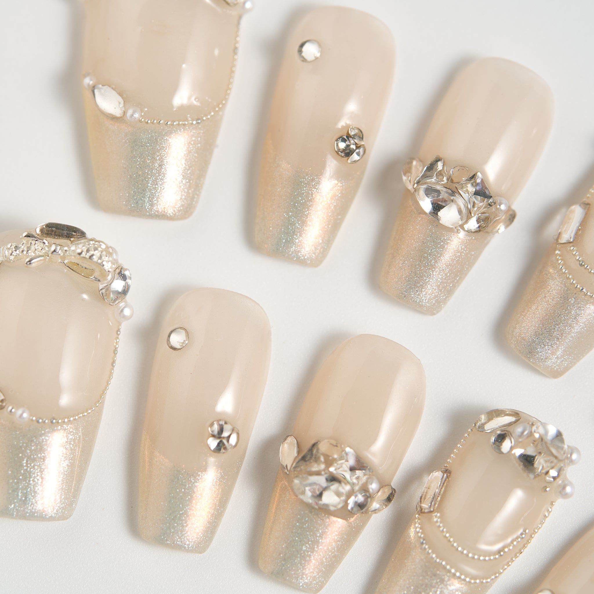 Close-up of Gilded Heiress beige press-on nails with crystal rhinestones and metallic shimmer on a white background.
