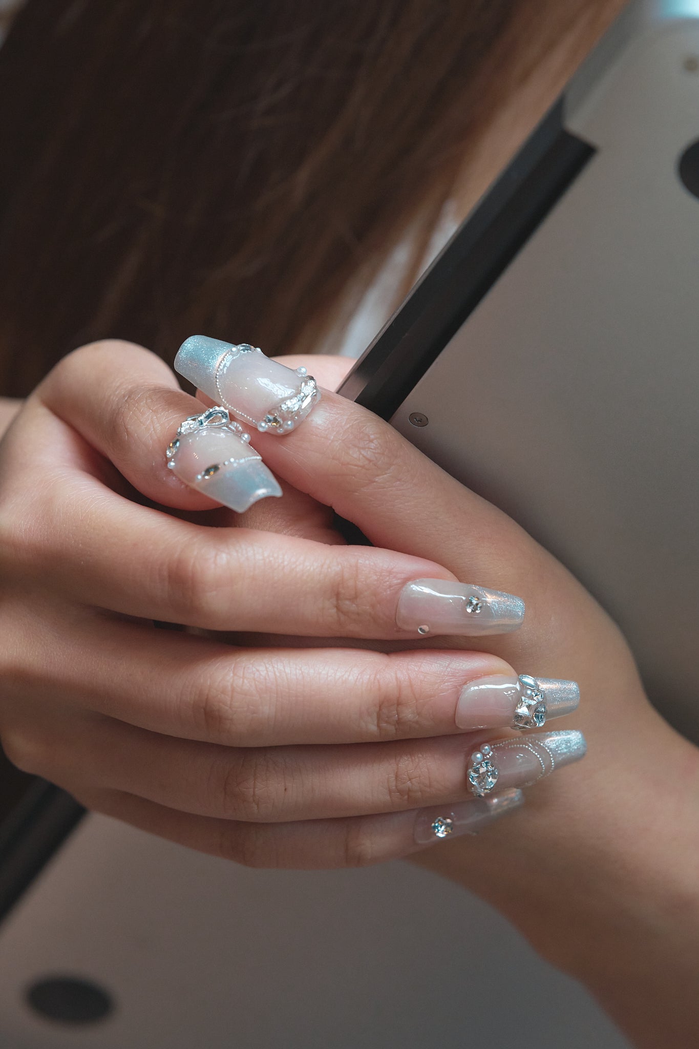 Close-up of a hand with Gilded Heiress rhinestone press-on nails holding a tablet.