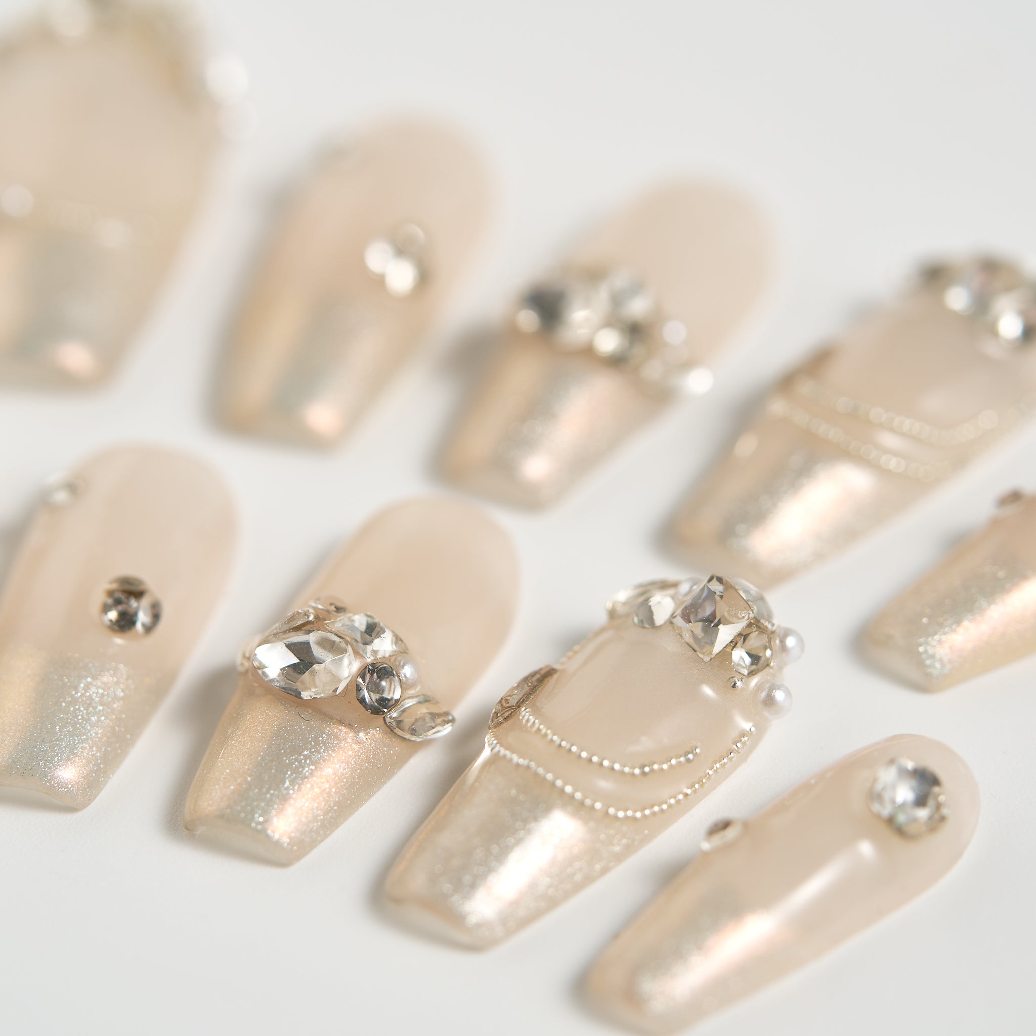 Angled view of Gilded Heiress press-on nails in beige with sparkling rhinestones and subtle shimmer, displayed on a white background.