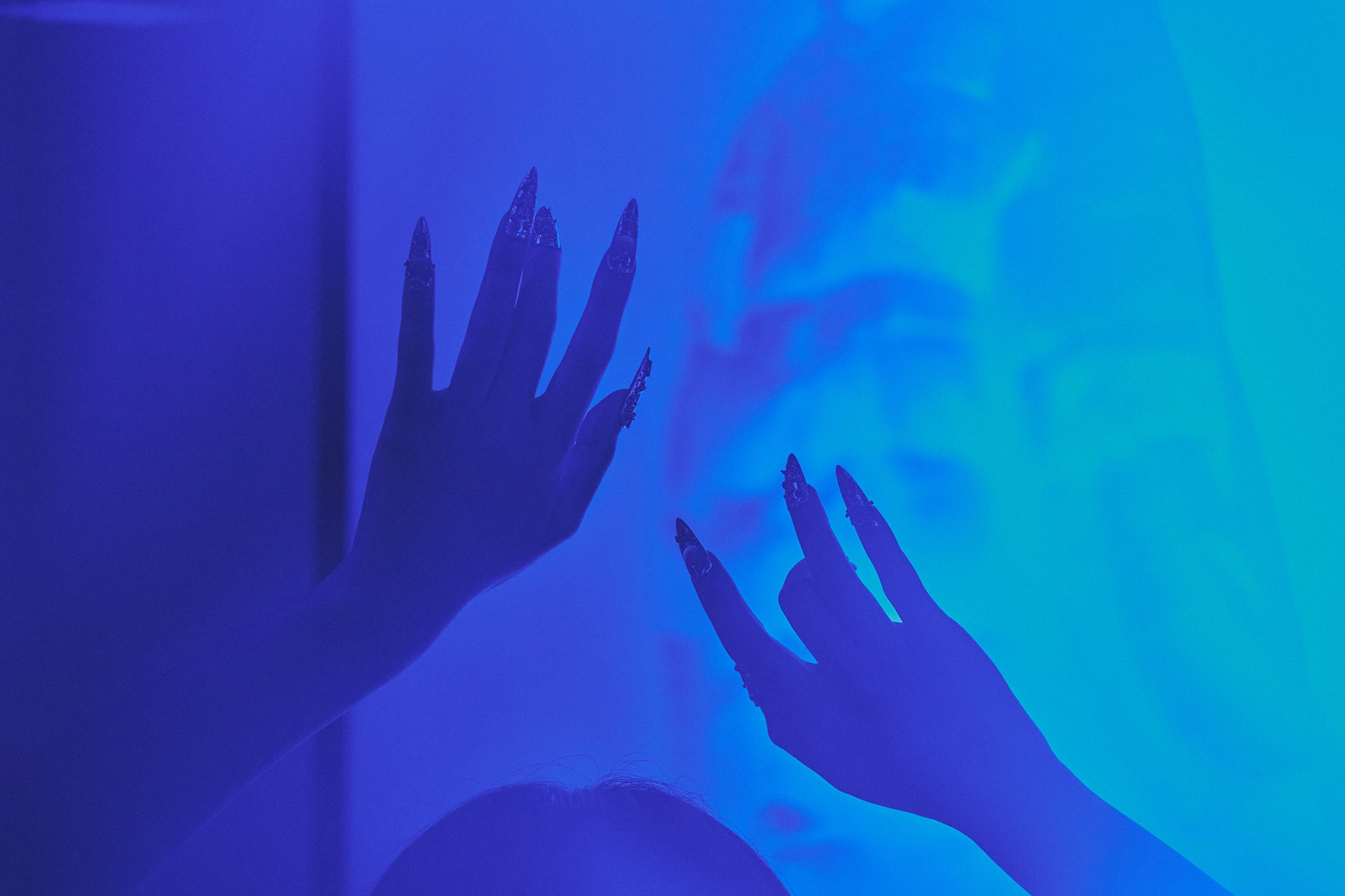 Chrome Reign stiletto press-on nails in metallic chrome silver, hands reaching in blue neon light, bold statement manicure for nightlife and club scene.