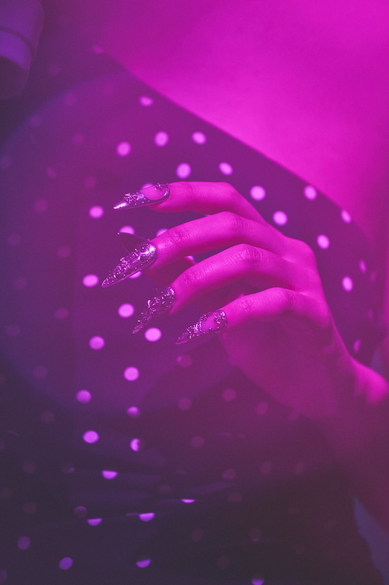 MiuNail Chrome Reign silver gothic nail art, hand in metallic 3D nails, polka dot dress, under vibrant purple lighting.