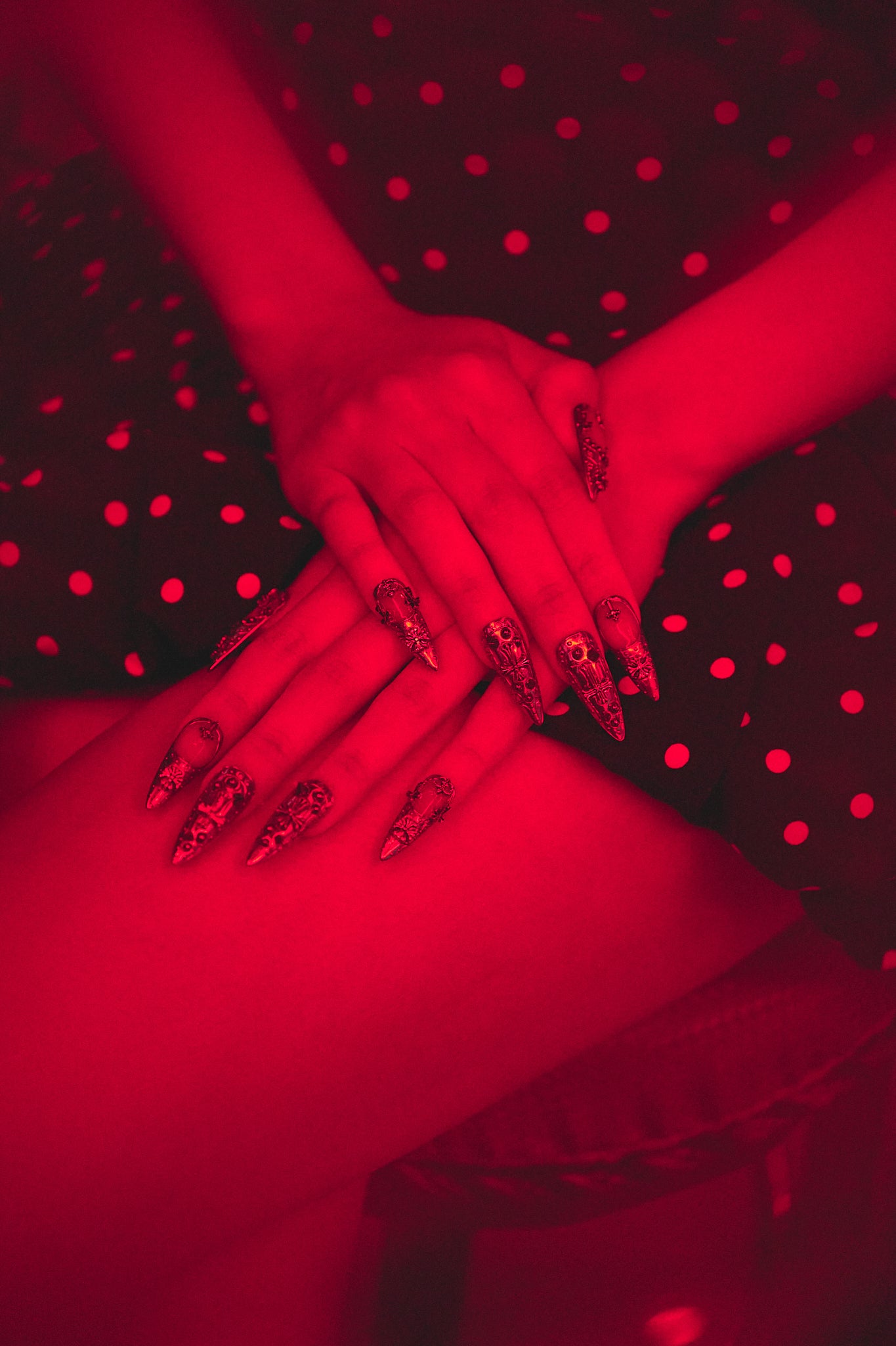 Chrome Reign stiletto press-on nails in metallic silver, both hands resting on polka dot dress, dramatic red nightclub lighting, bold edgy manicure style.
