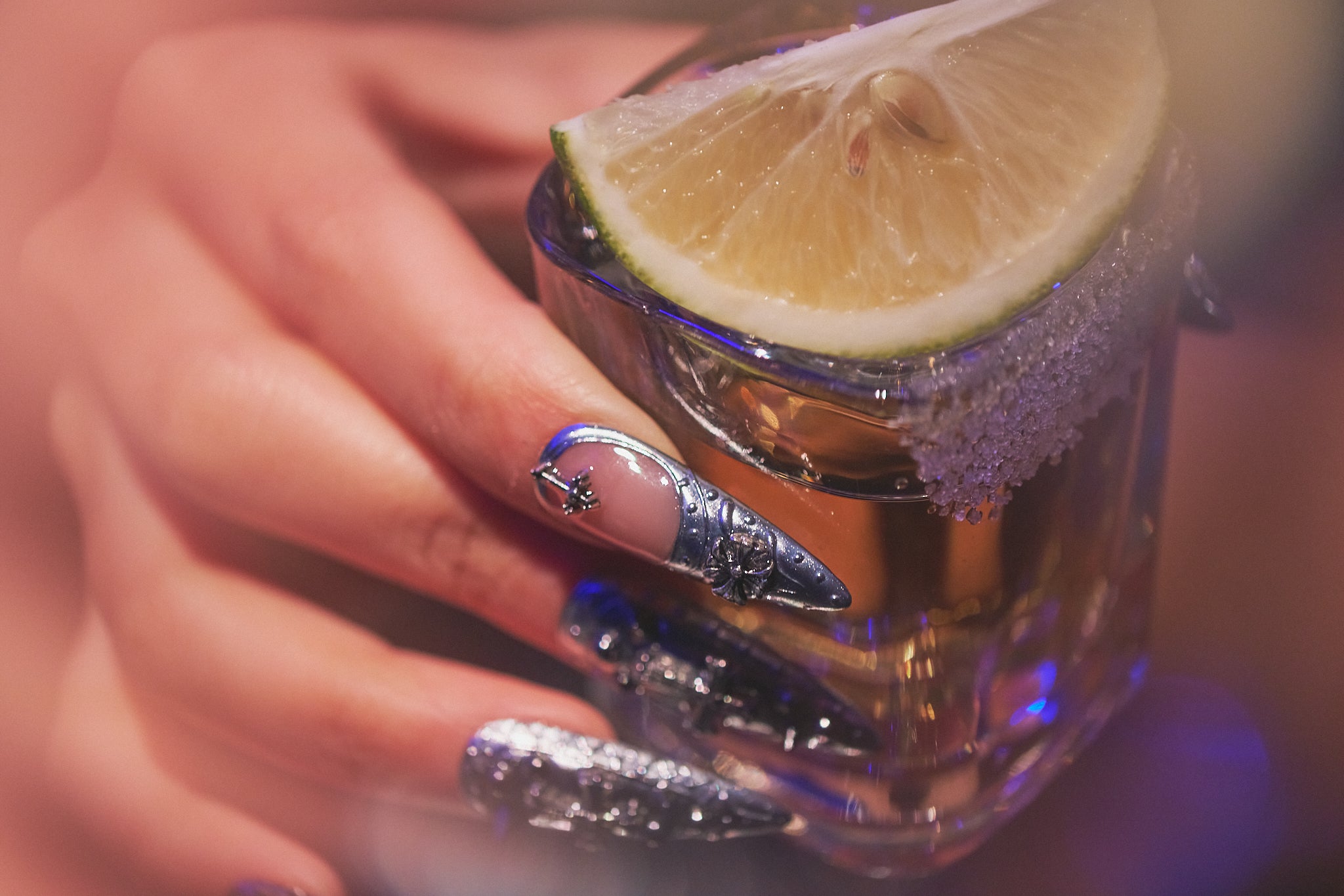 MiuNail Chrome Reign stiletto press-on nails in metallic chrome silver, hand holding a tequila shot with lime wedge, salon-quality reusable nails for nightlife.