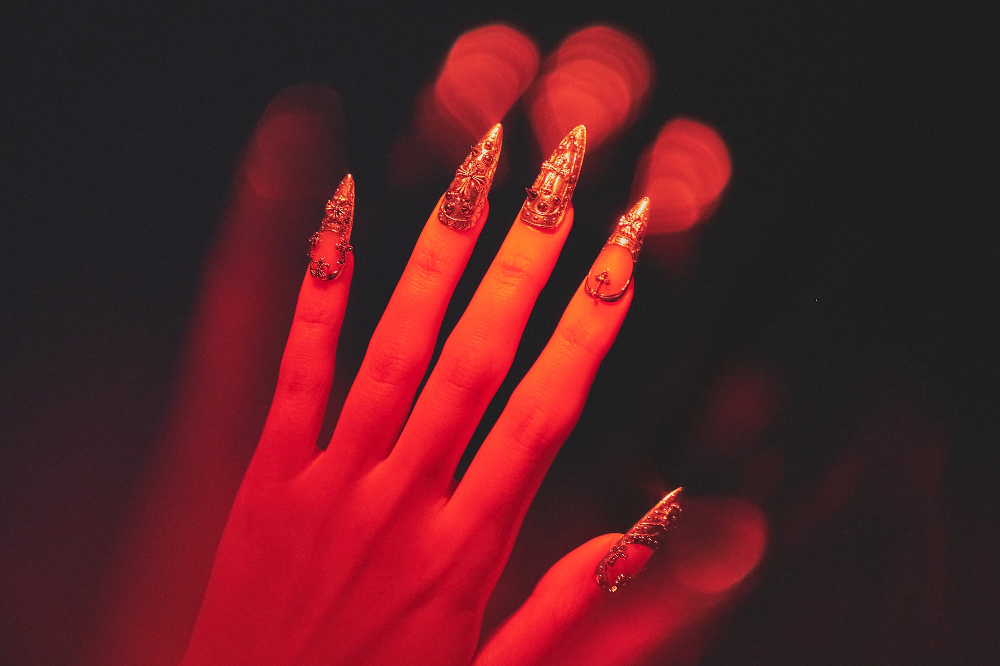 Chrome Reign stiletto press-on nails in metallic chrome silver, hand illuminated by red nightclub lighting, salon-quality reusable nails for party looks.