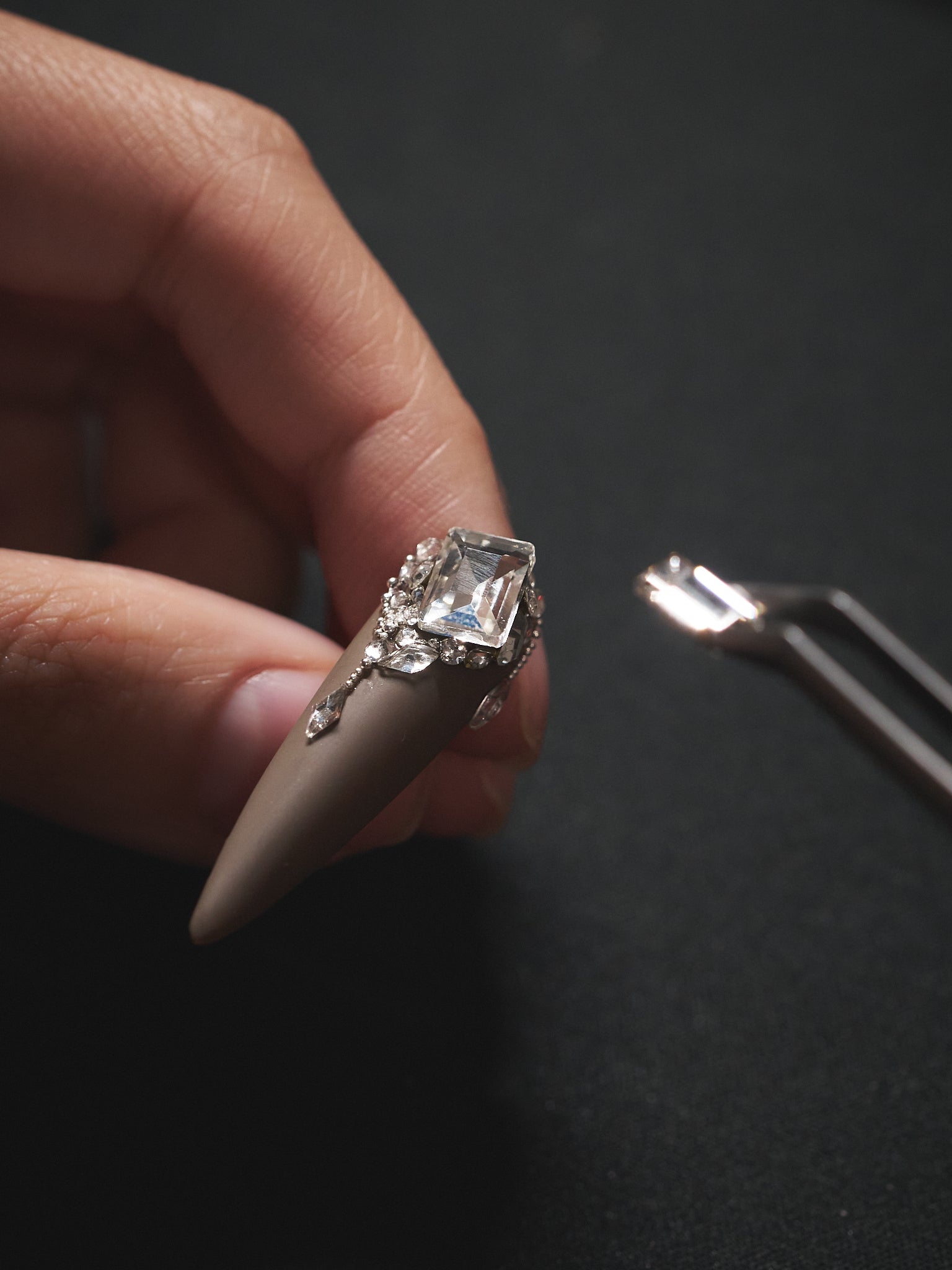 Artist hand-finishing a MiuNail “Desert Halo” matte press-on nail with a large rhinestone, demonstrating expert craftsmanship and detailed artistry.