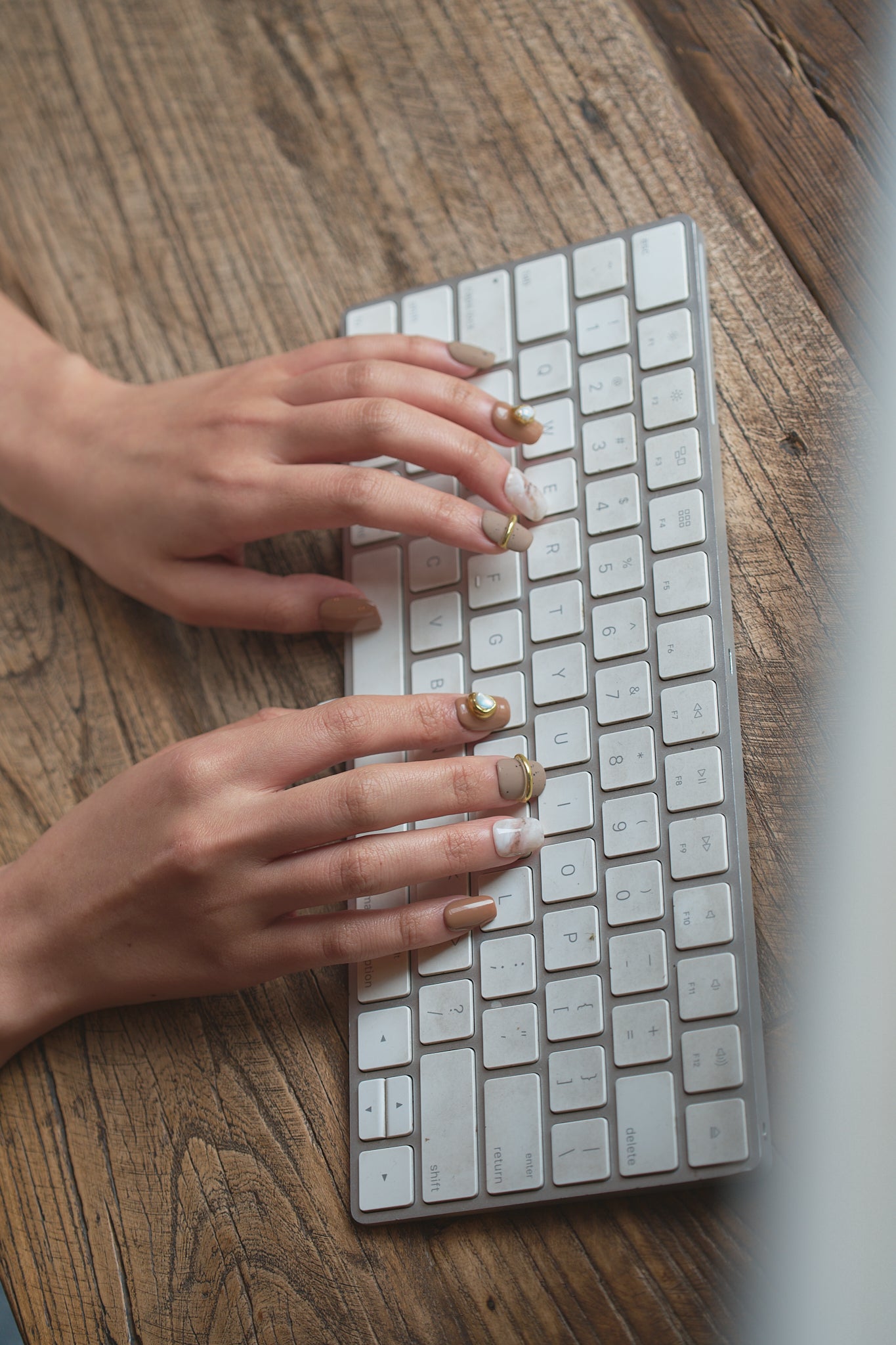 Hands wearing MiuNail Golden Dune press-on nails in marble, brown, and gold, typing on a white wireless keyboard on a wooden desk.