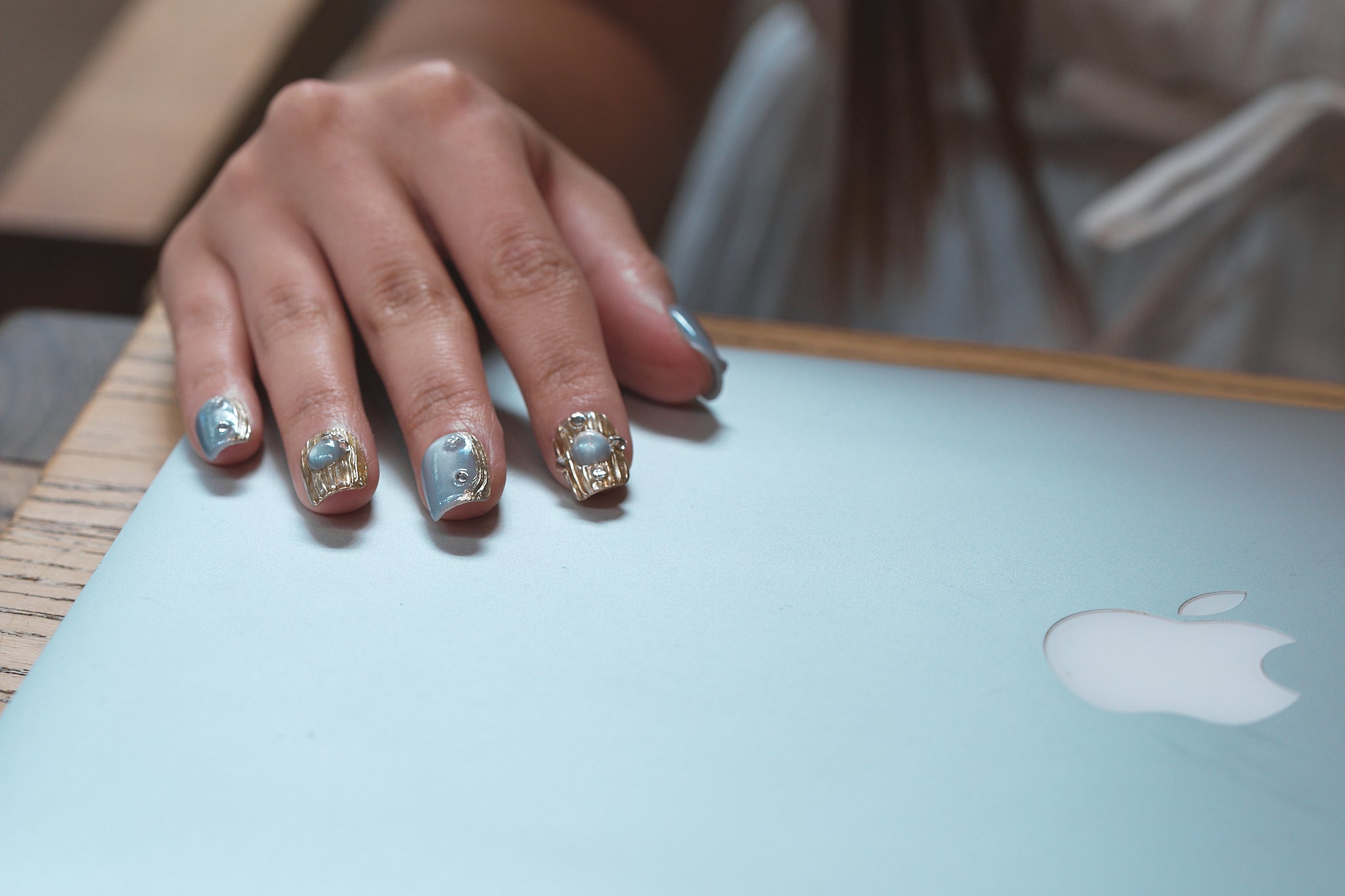 Hand with MiuNail Mist Orbit press-on nails in silver and gold resting on a closed laptop.