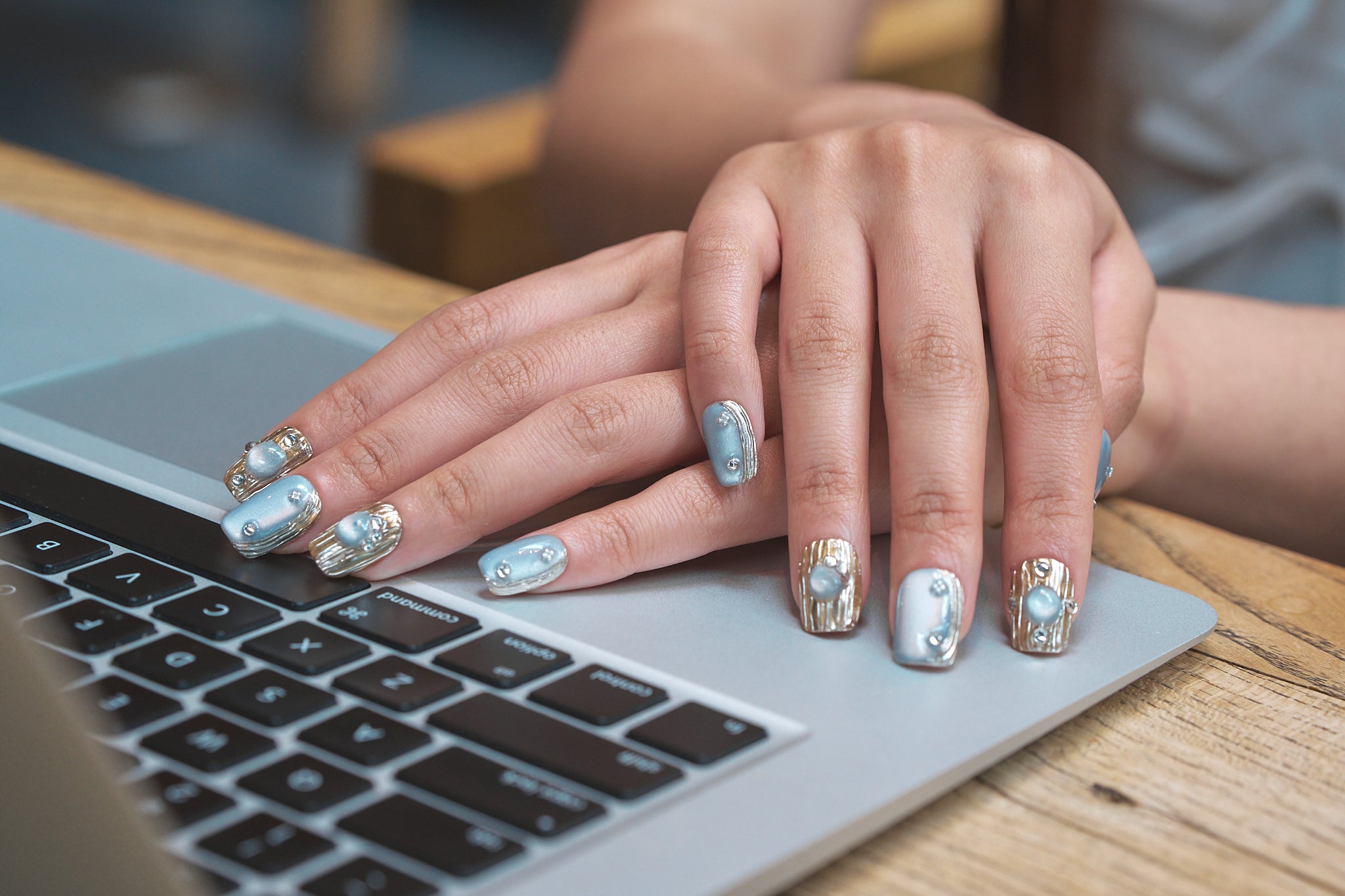 Hands featuring MiuNail Mist Orbit metallic press-on nails in silver and gold, resting on a laptop keyboard.