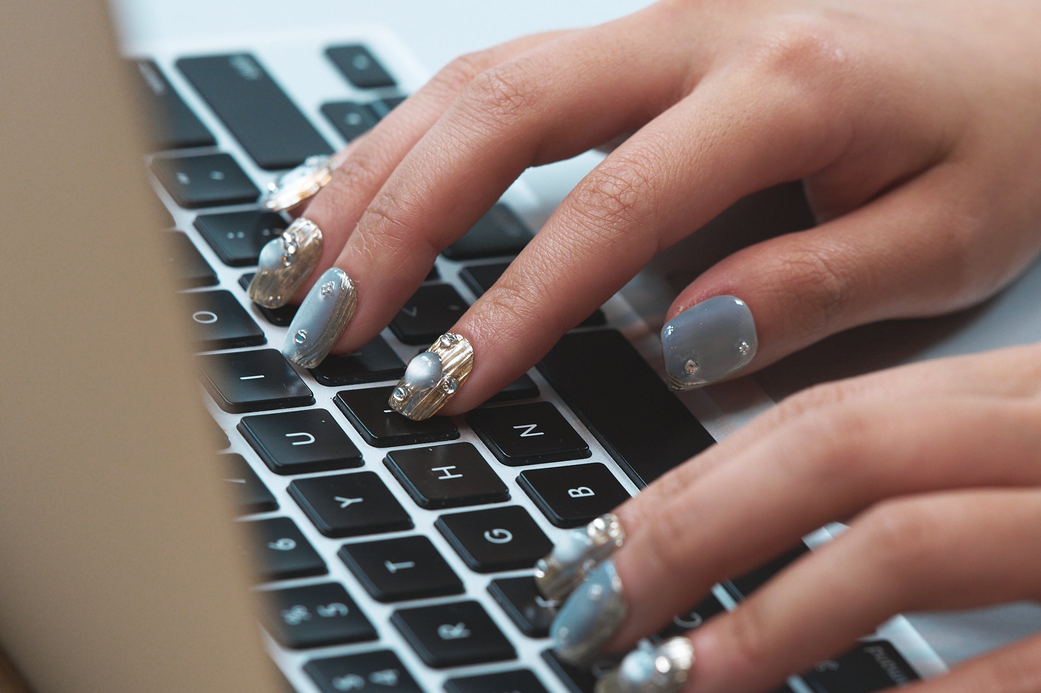 Close-up of hands with MiuNail Mist Orbit metallic press-on nails typing on a laptop keyboard.