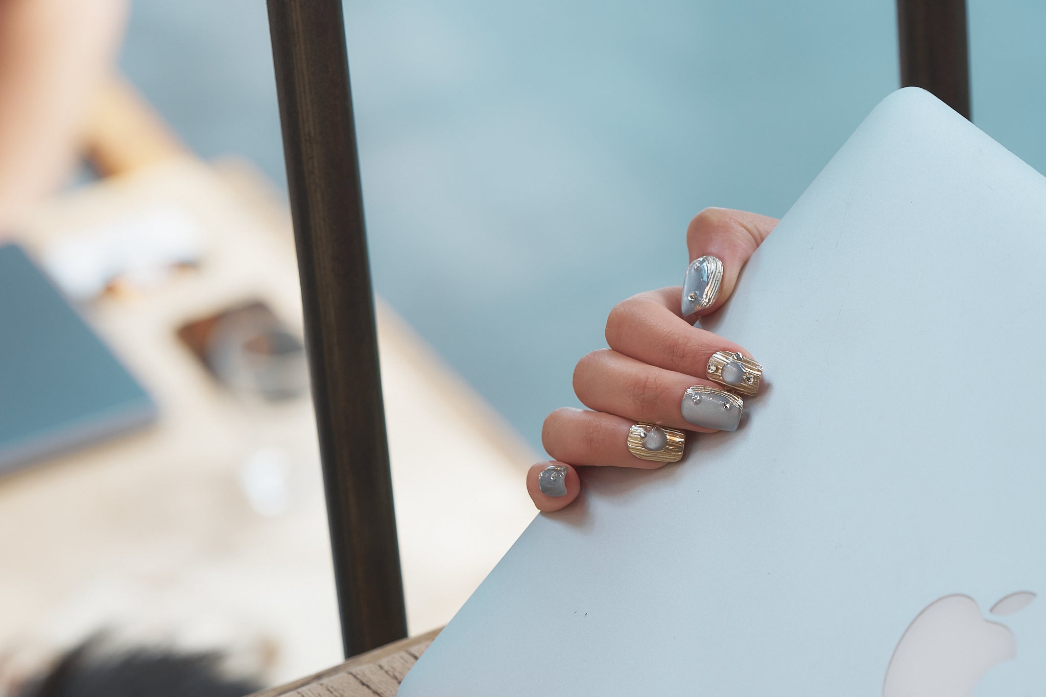 Hand with MiuNail Mist Orbit metallic press-on nails holding a closed laptop outdoors.