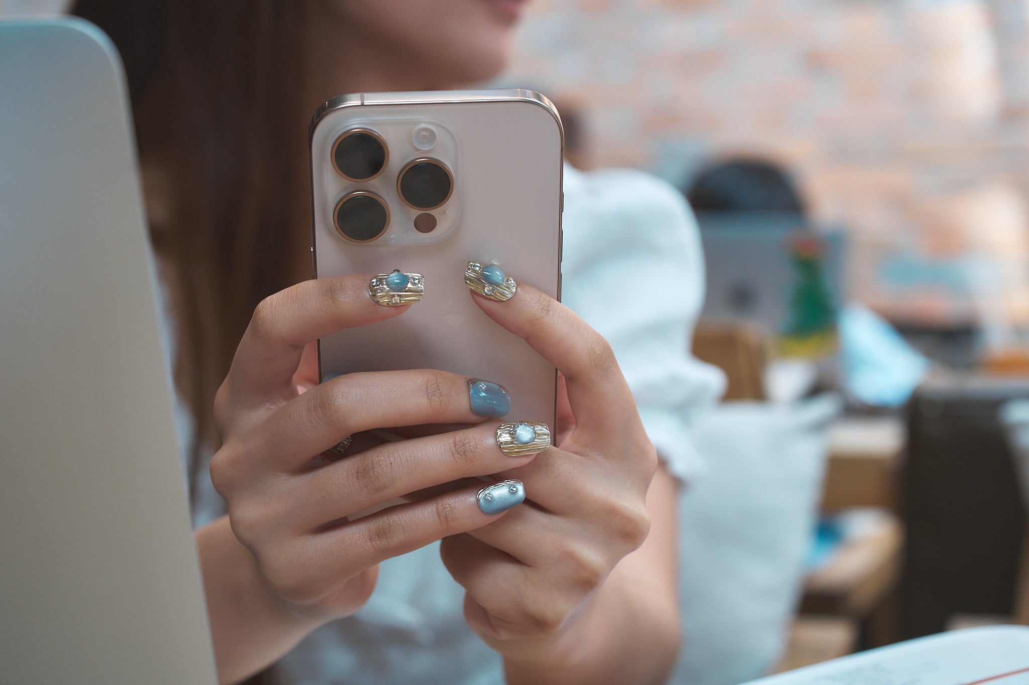 Hands with MiuNail Mist Orbit metallic press-on nails holding a smartphone indoors.