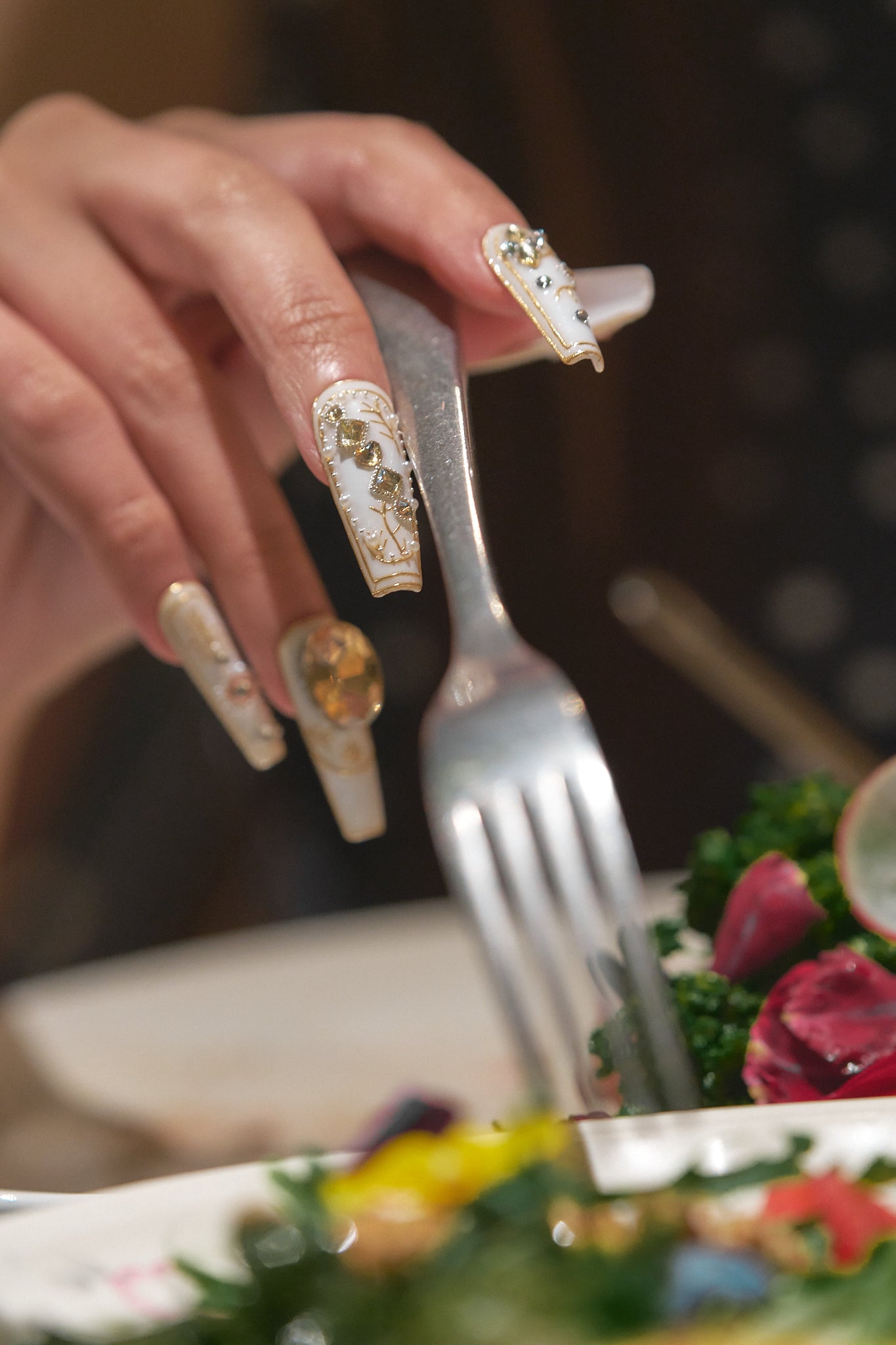 Close-up of a hand with elegant white and gold nail art holding a fork above a fresh salad.