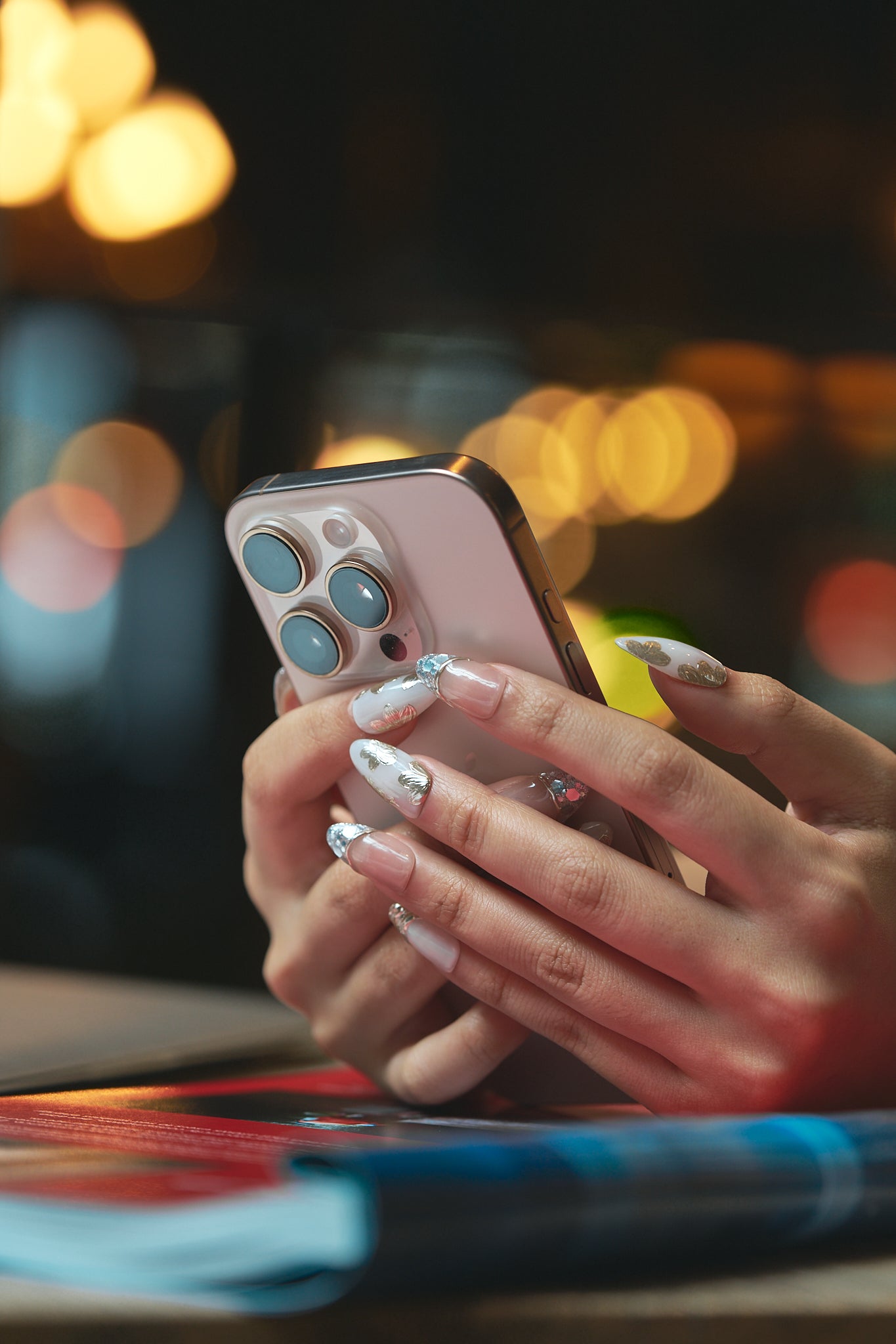 Hand with MiuNail “Petal Bloom” floral press-on nails holding a smartphone, with a soft bokeh background.