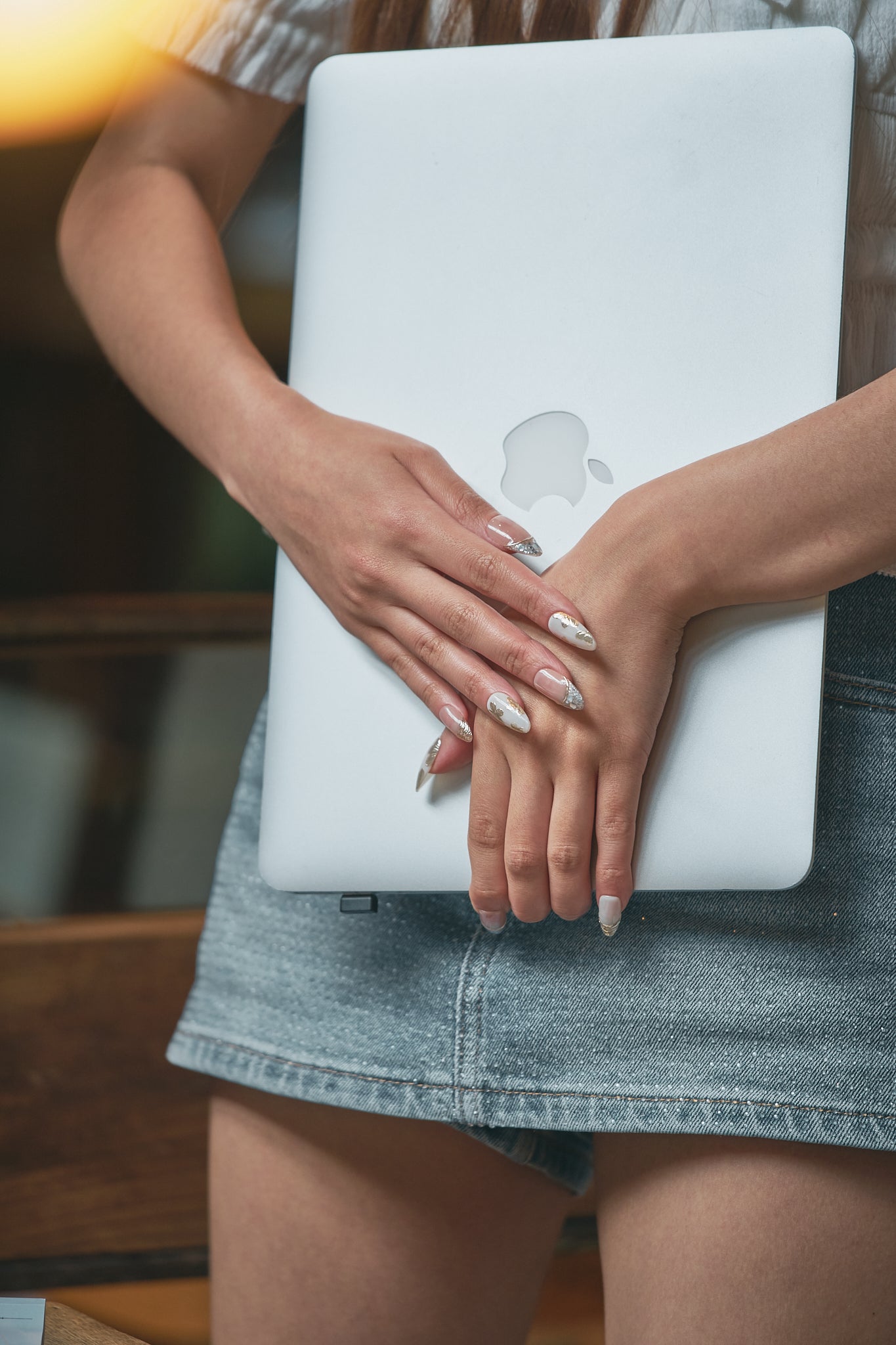 Petal Bloom long almond press-on nails in marble white and gold, hands holding a white laptop, denim skirt, blurred background