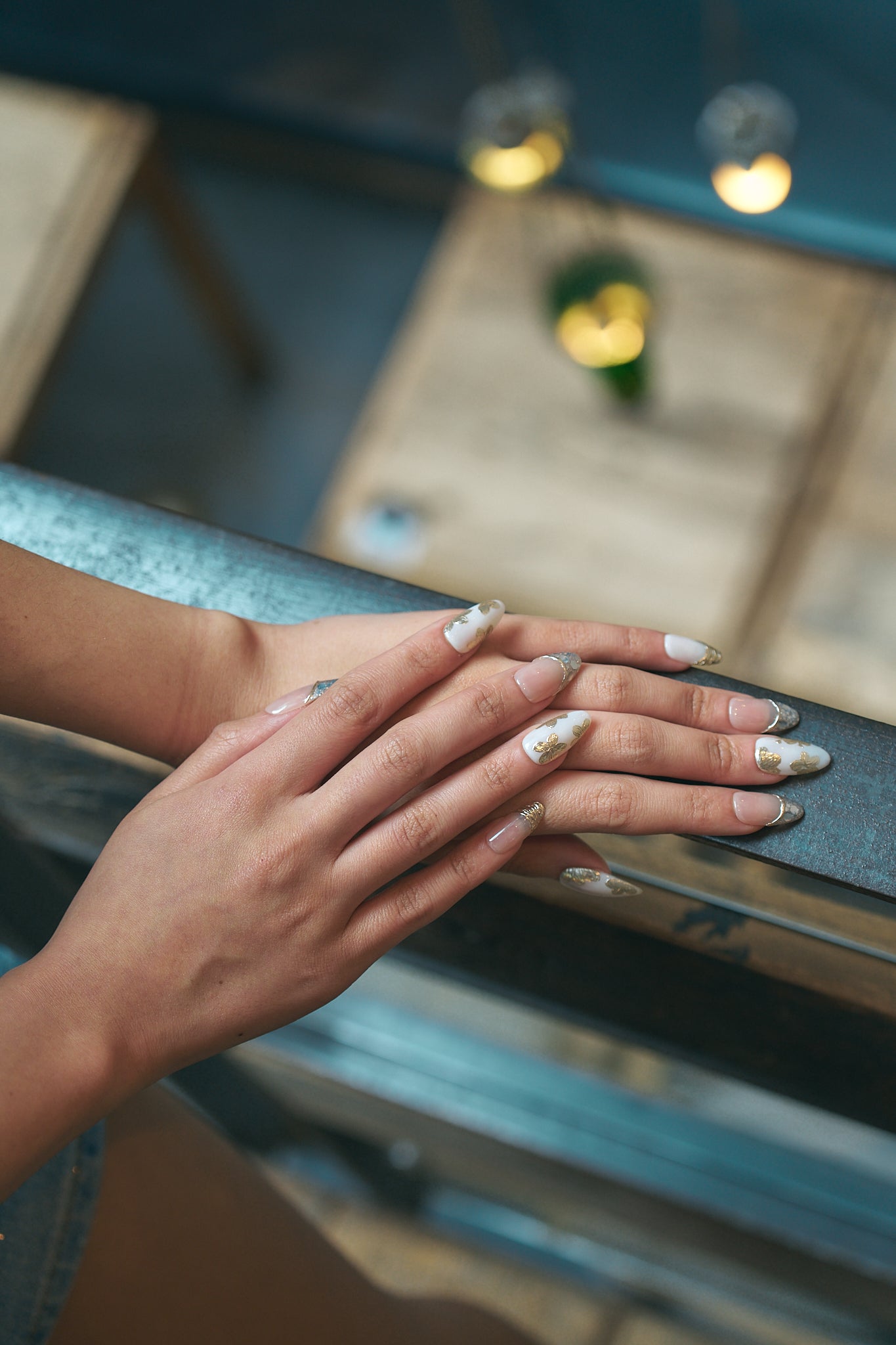 Petal Bloom long almond press-on nails in marble white and gold, worn on hands over a metallic railing