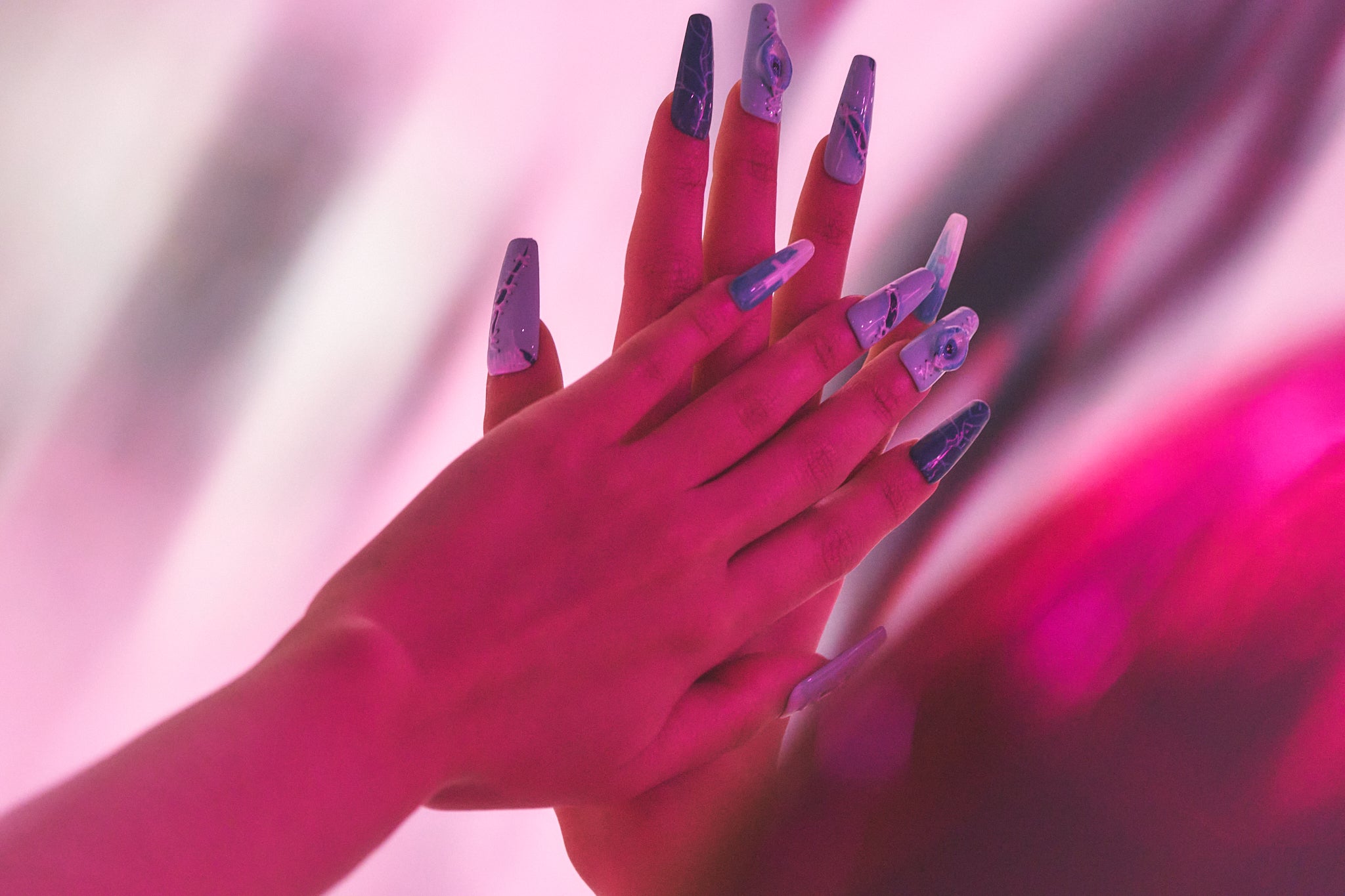 Hands wearing MiuNail Siren Hex press-on nails in electric blue and white, pressed together under pink and purple lighting.