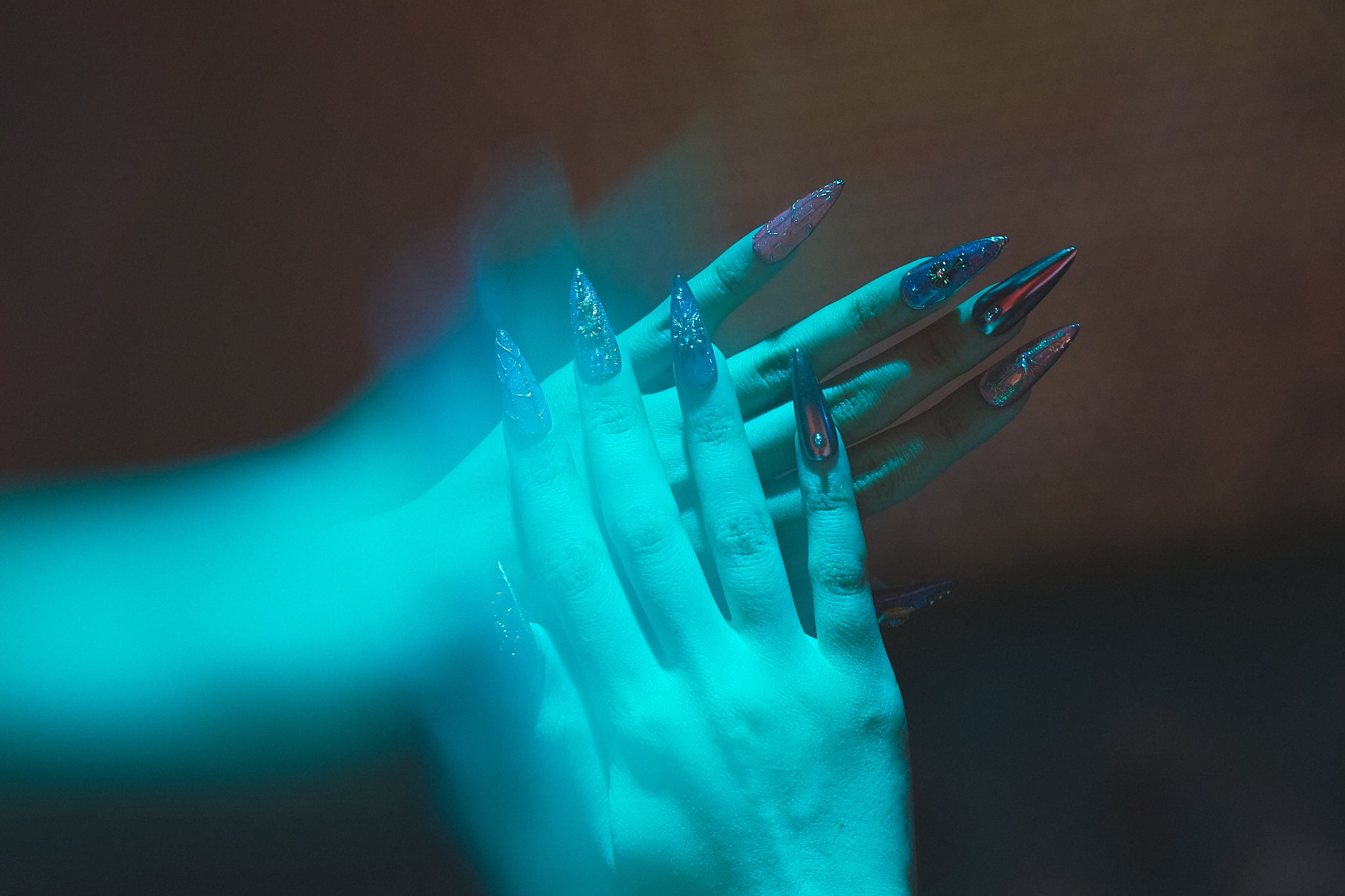 Violet Eclipse stiletto press-on nails in metallic purple and gold, hands illuminated by blue lighting