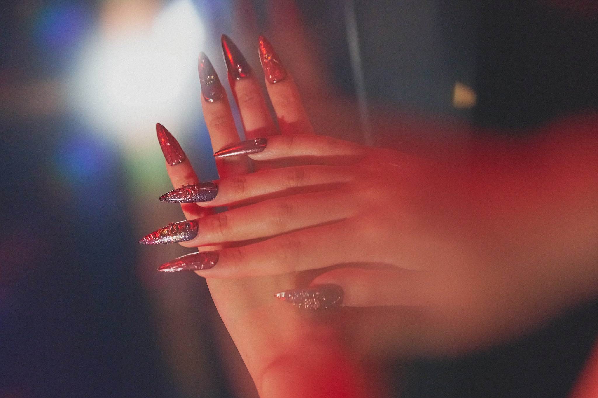 Violet Eclipse stiletto press-on nails in metallic purple and gold, hands posed together under red club lights, salon-quality nails