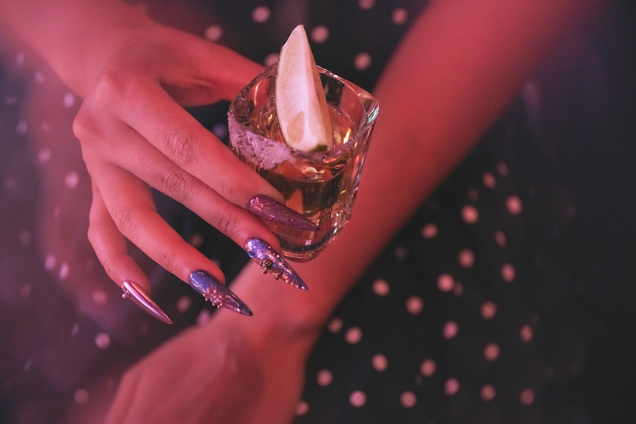 Violet Eclipse stiletto press-on nails in metallic purple and gold, hand holding a tequila shot with lemon wedge, instant manicure for parties