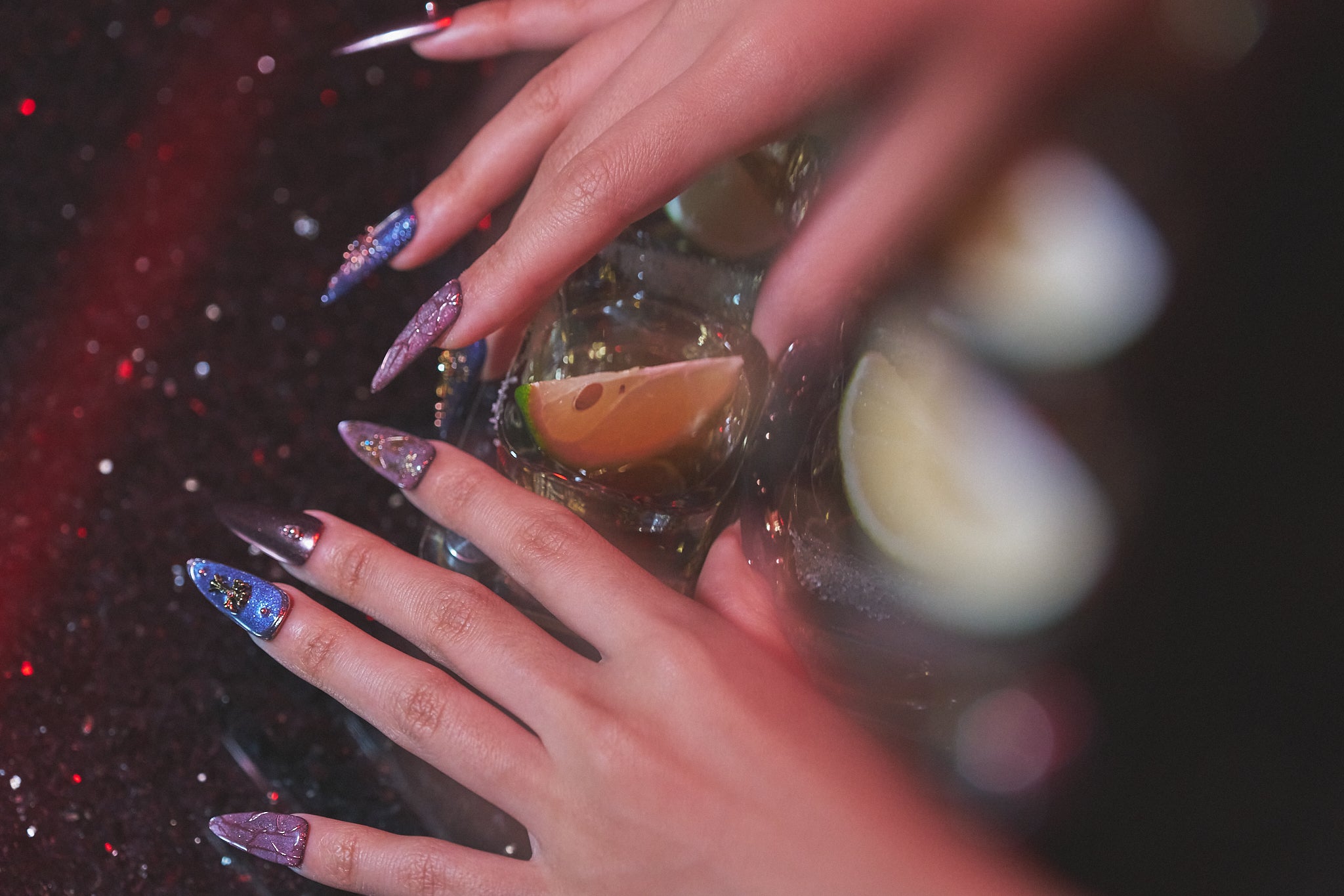 Violet Eclipse metallic purple and gold stiletto press-on nails, both hands beside tequila shots with lemon wedges on a bar counter