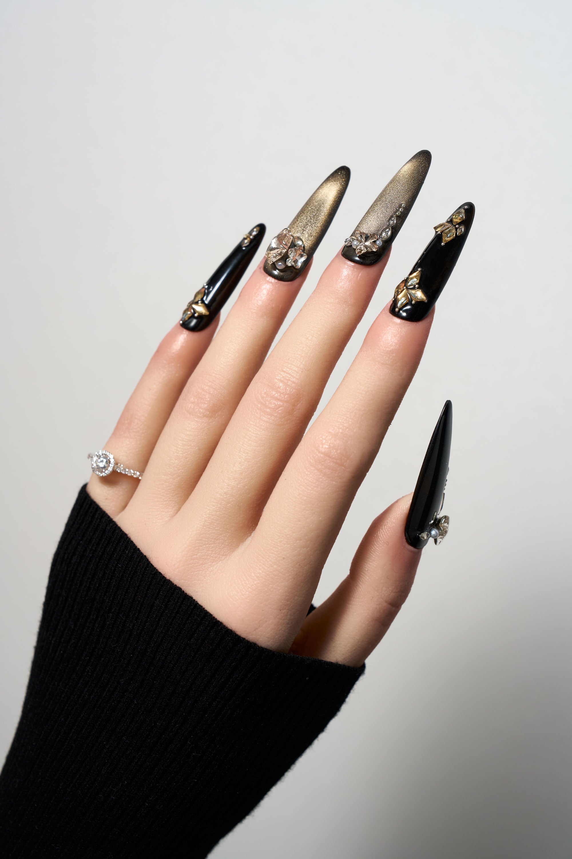 Nocturne Aurum reusable stiletto press-on nails featuring a sophisticated black and gold theme with cat-eye shimmer, 3D gold butterfly accents, and sparkling crystal clusters.