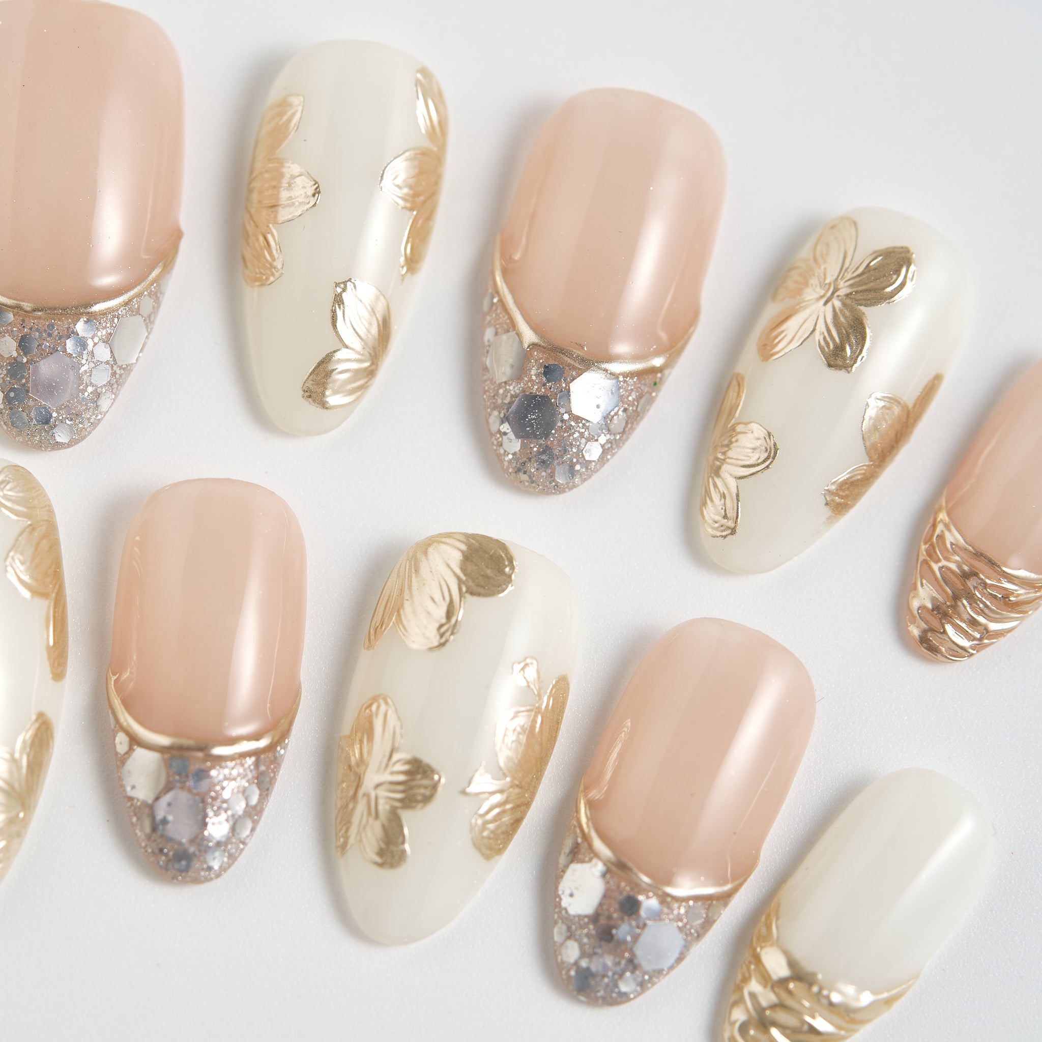 Close-up of Petal Bloom press-on nails with beige and gold designs on a white background.