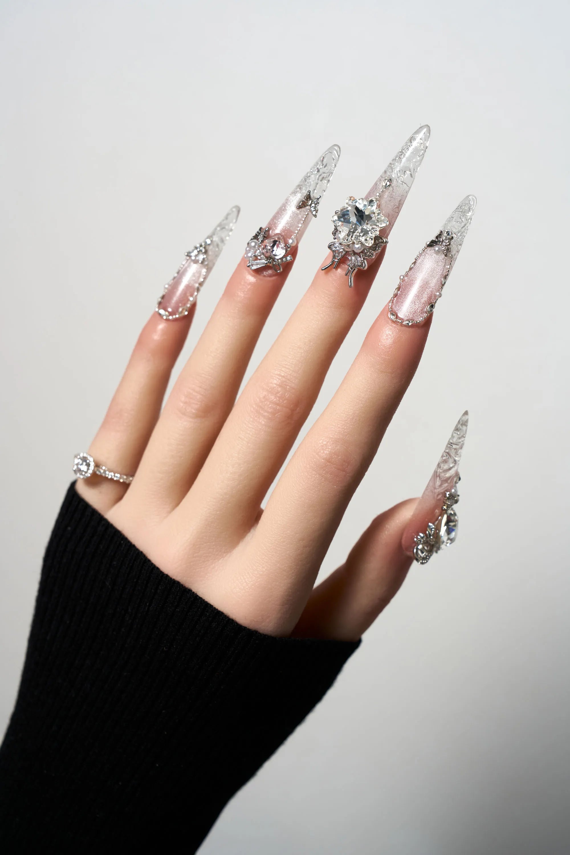 Rosé Glacé reusable extra-long stiletto press-on nails showcasing a sheer pink cat-eye shimmer, decorated with delicate white ribbon bows, 3D silver heart charms, and dangling crystal teardrop accents.