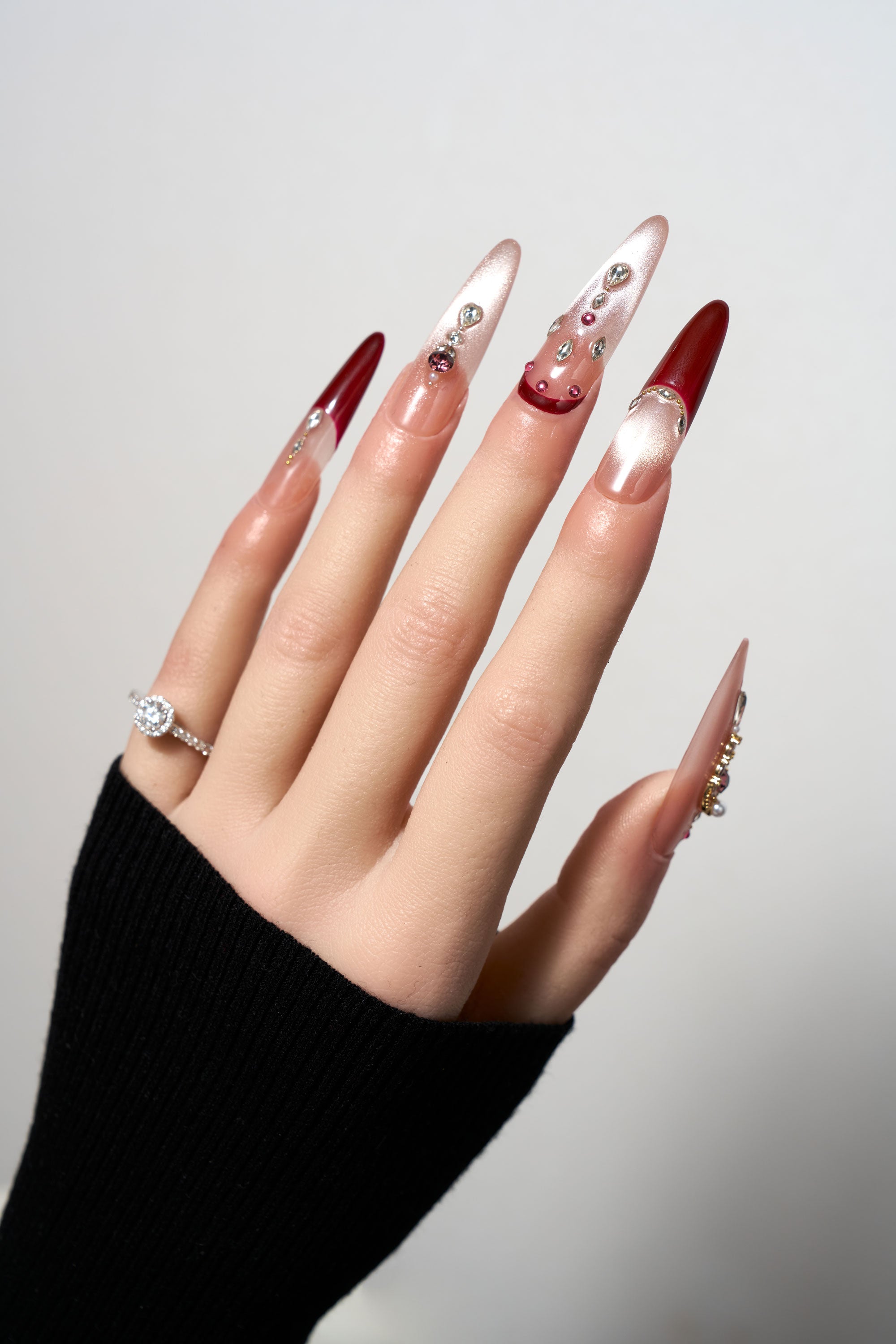 Royal Garnet reusable extra-long stiletto press-on nails featuring a mix of deep burgundy red and silvery cat-eye shimmer, adorned with pink and crystal gemstones.