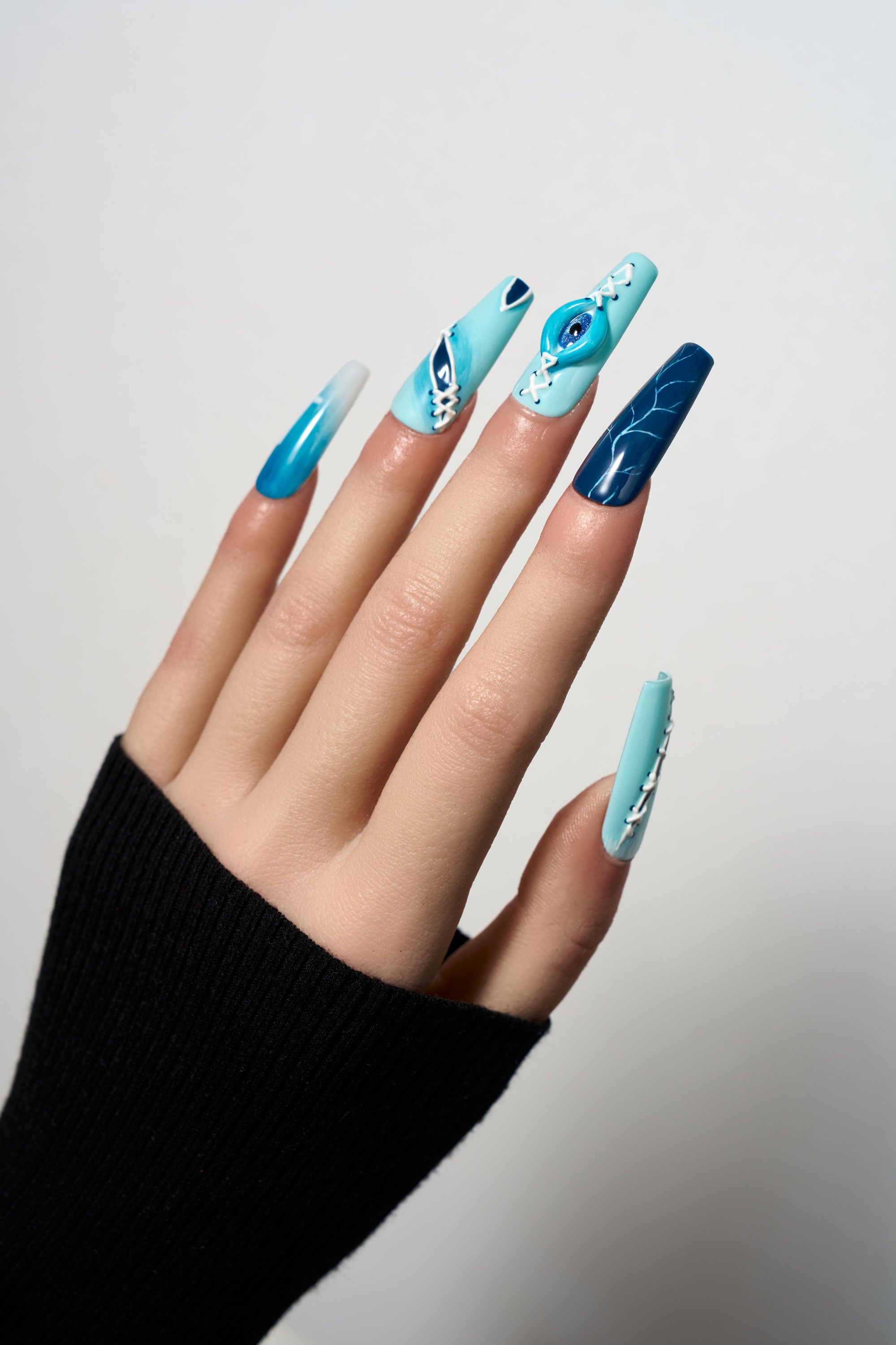 Siren Hex medium coffin press-on nails featuring a blue and teal gradient, lightning bolt textures, and a dramatic 3D evil eye charm with corset-style white lacing details.