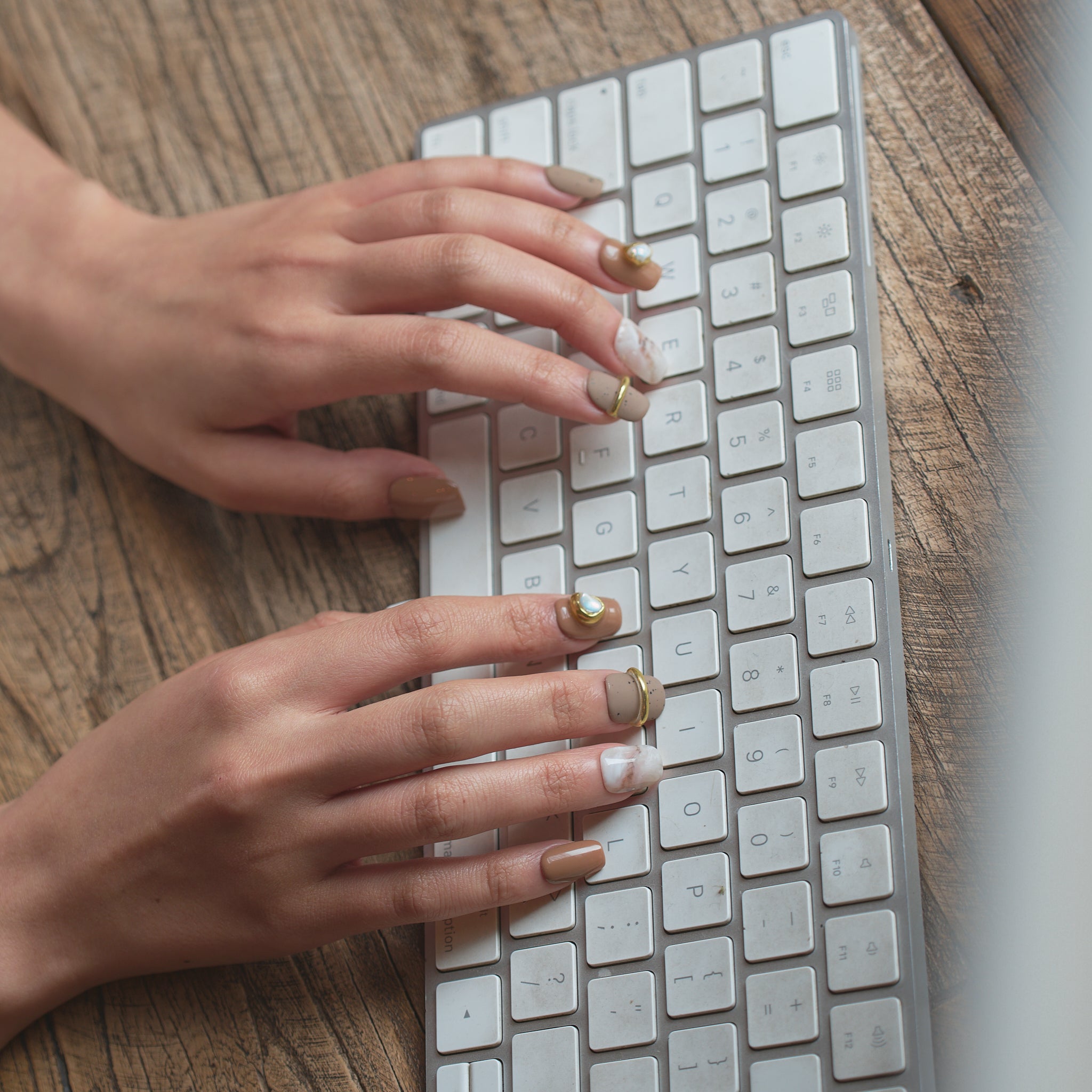 Hand wearing MiuNail EASE collection Golden Dune press-on nails, typing on a white computer keyboard, showing a minimalist, everyday look.