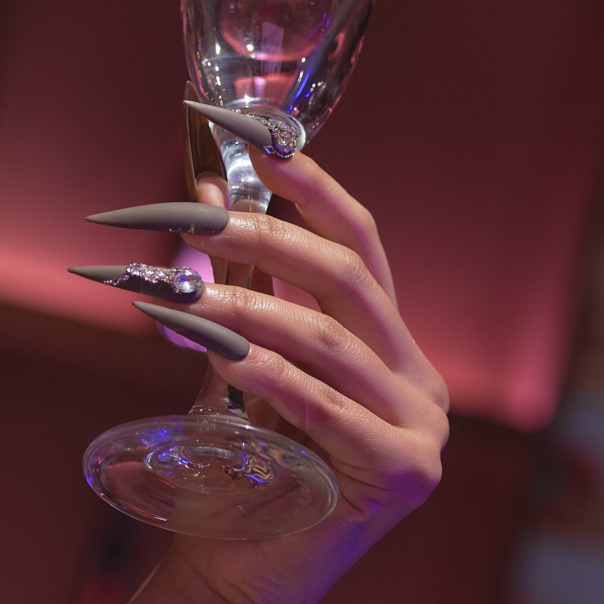 Hand showcasing MiuNail GALA collection Desert Halo press-on nails, holding a wine glass under elegant, moody lighting.