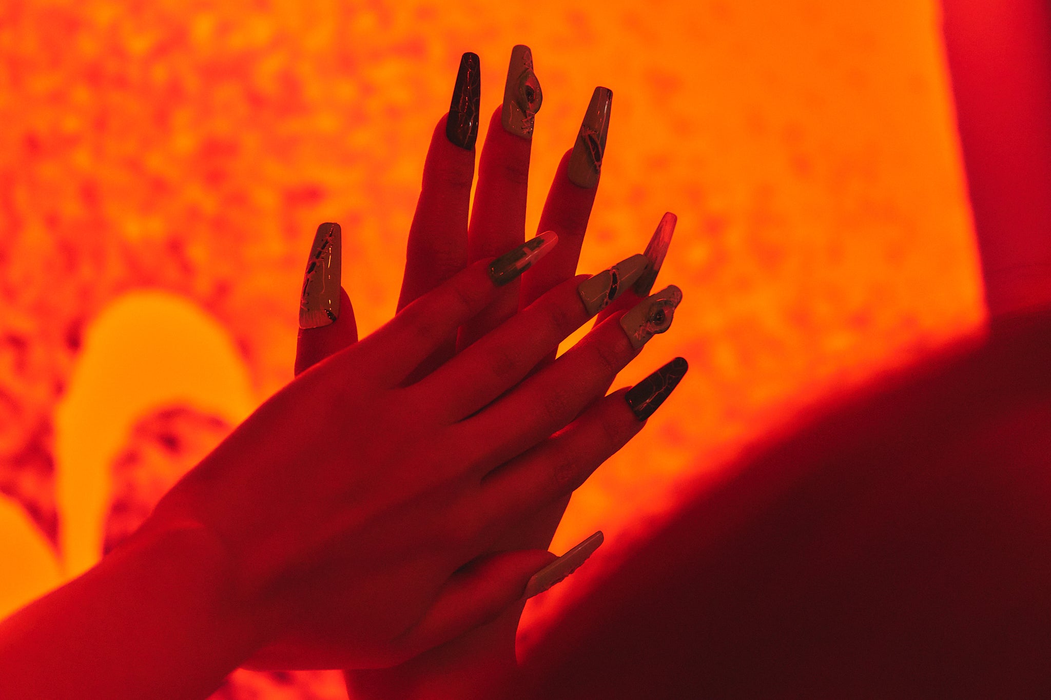 Hands wearing MiuNail Siren Hex press-on nails in deep blue and white, layered against a vivid orange backdrop.