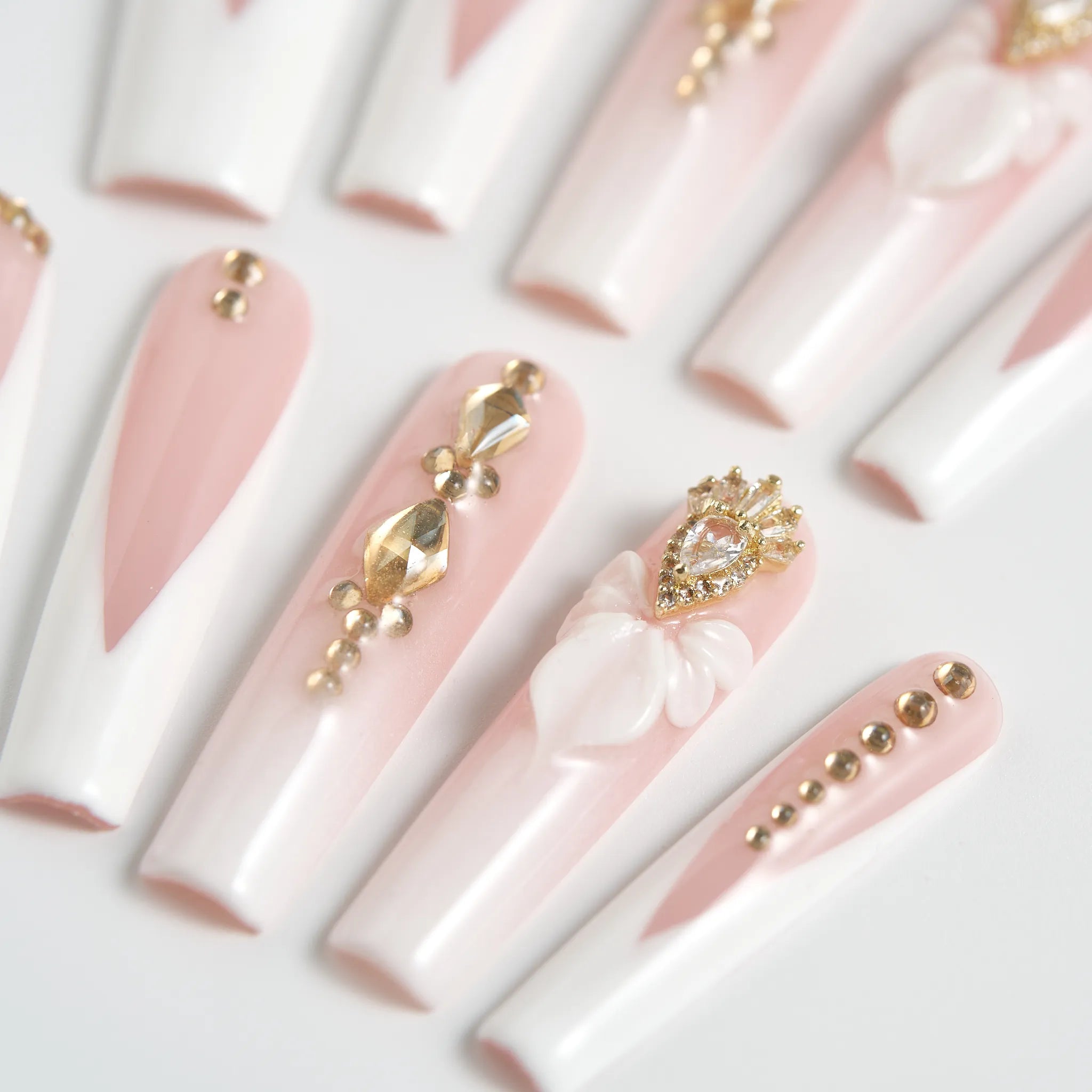 Decorative false nails with pink and gold designs on a white background