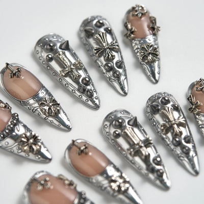 Decorative nail art with silver embellishments and beige nail polish on a white background