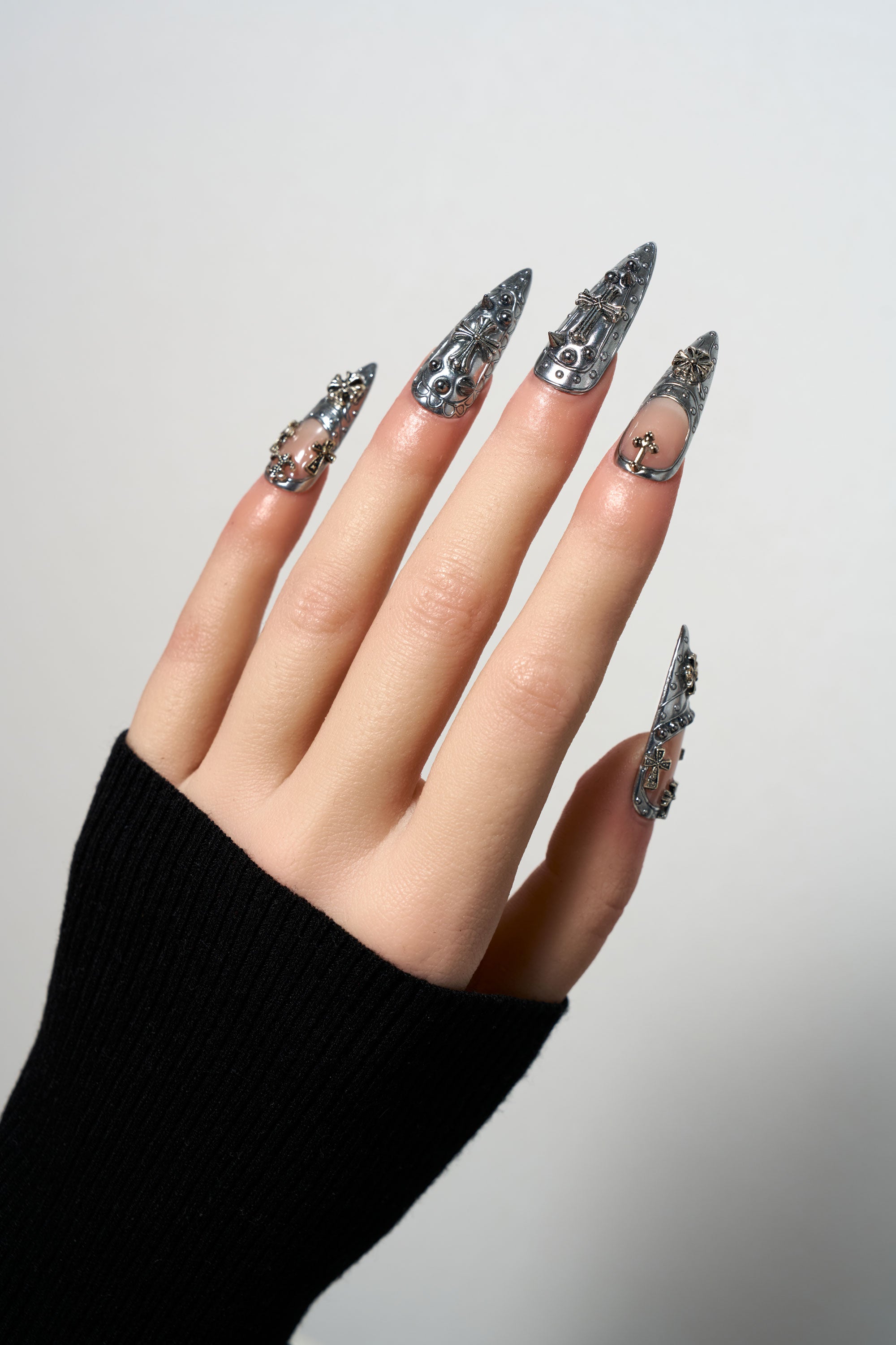 Chrome Reign reusable stiletto press-on nails with a high-shine silver metallic finish, featuring intricate gothic embossed patterns, 3D silver cross charms, and punk-style rivet details.