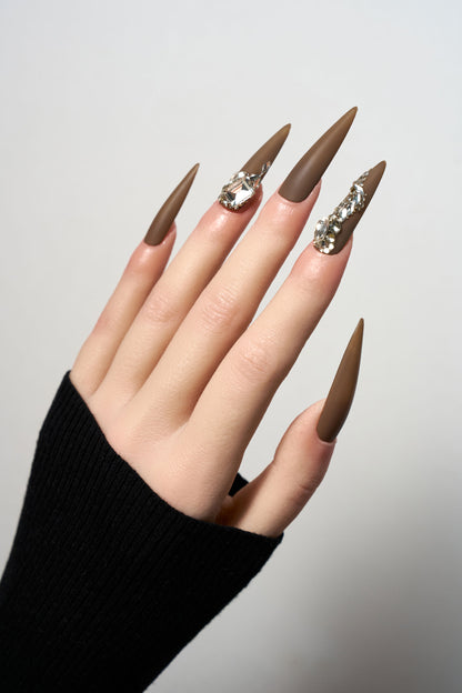 Desert Halo reusable long stiletto press-on nails in a sophisticated matte chocolate brown finish, heavily adorned with luxury clear crystal trails and large focal gemstones.
