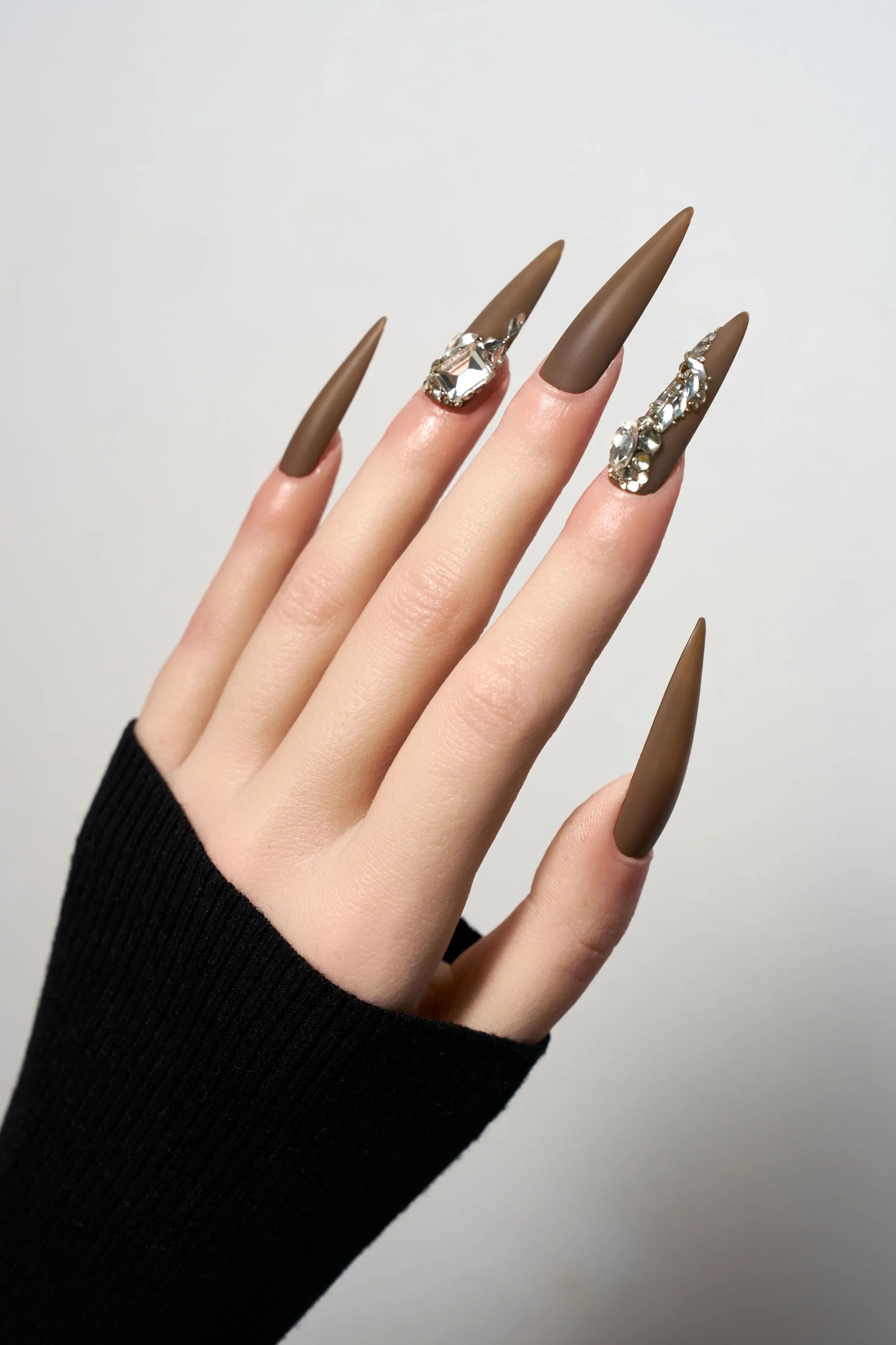 Desert Halo reusable long stiletto press-on nails in a sophisticated matte chocolate brown finish, heavily adorned with luxury clear crystal trails and large focal gemstones.