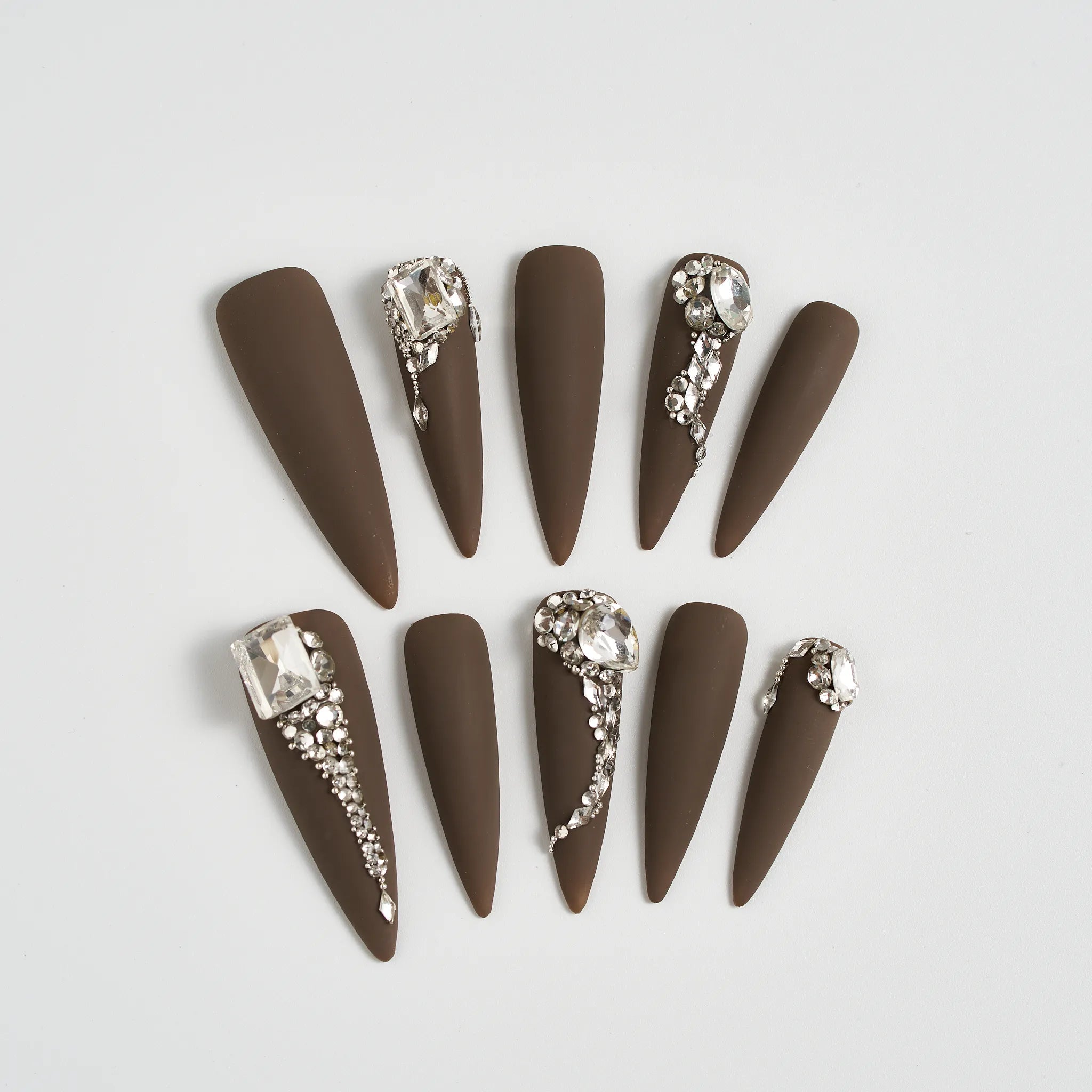 Brown nail art designs with rhinestone accents on a light gray background